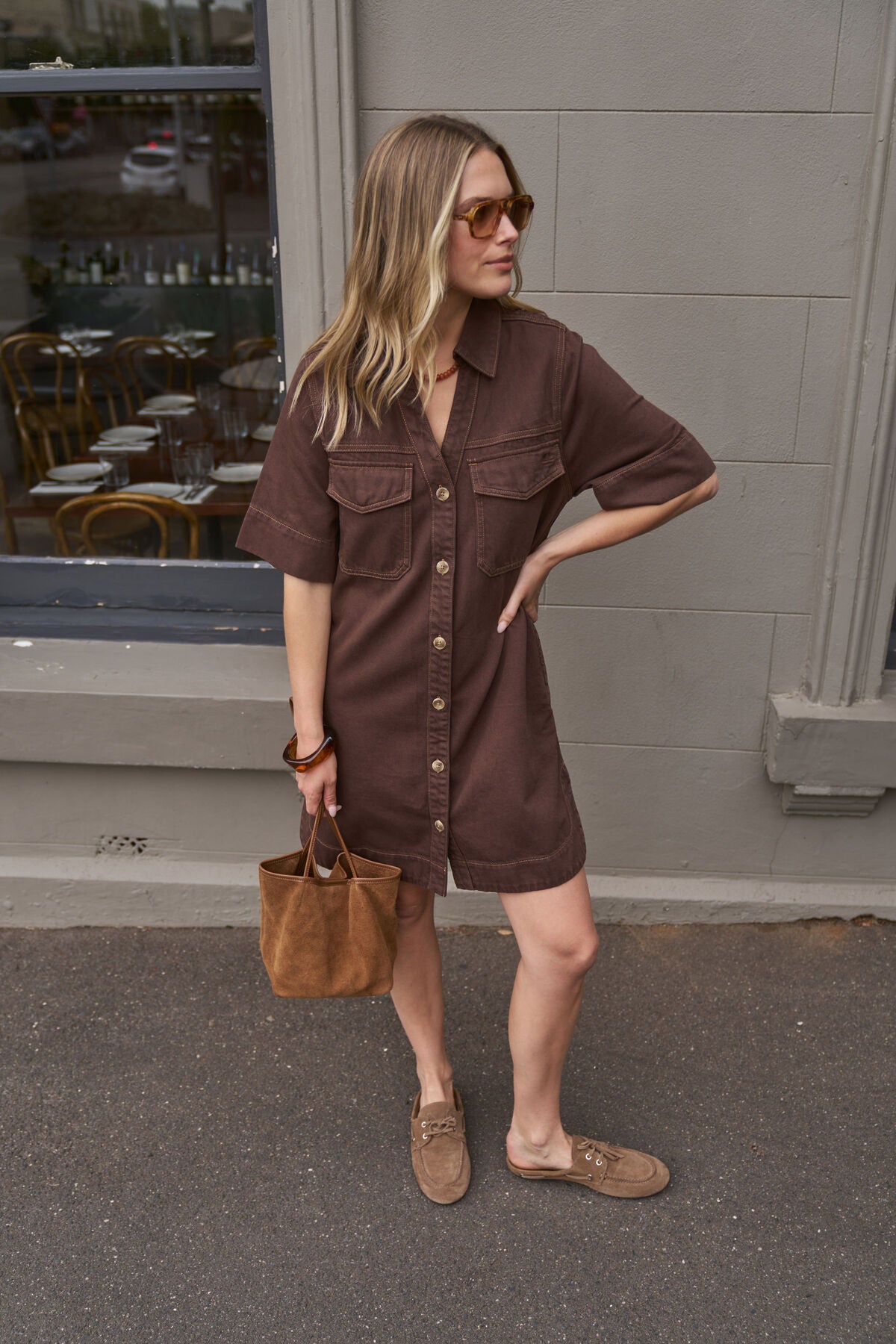 Woman wearing a Ceres Life brown dress with a handbag standing outside a building.