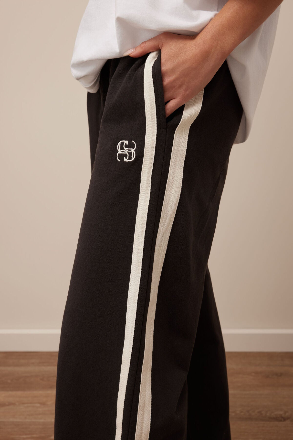 Image of Ceres Life black track pants with a white stripe and logo worn by a person, against a plain background.