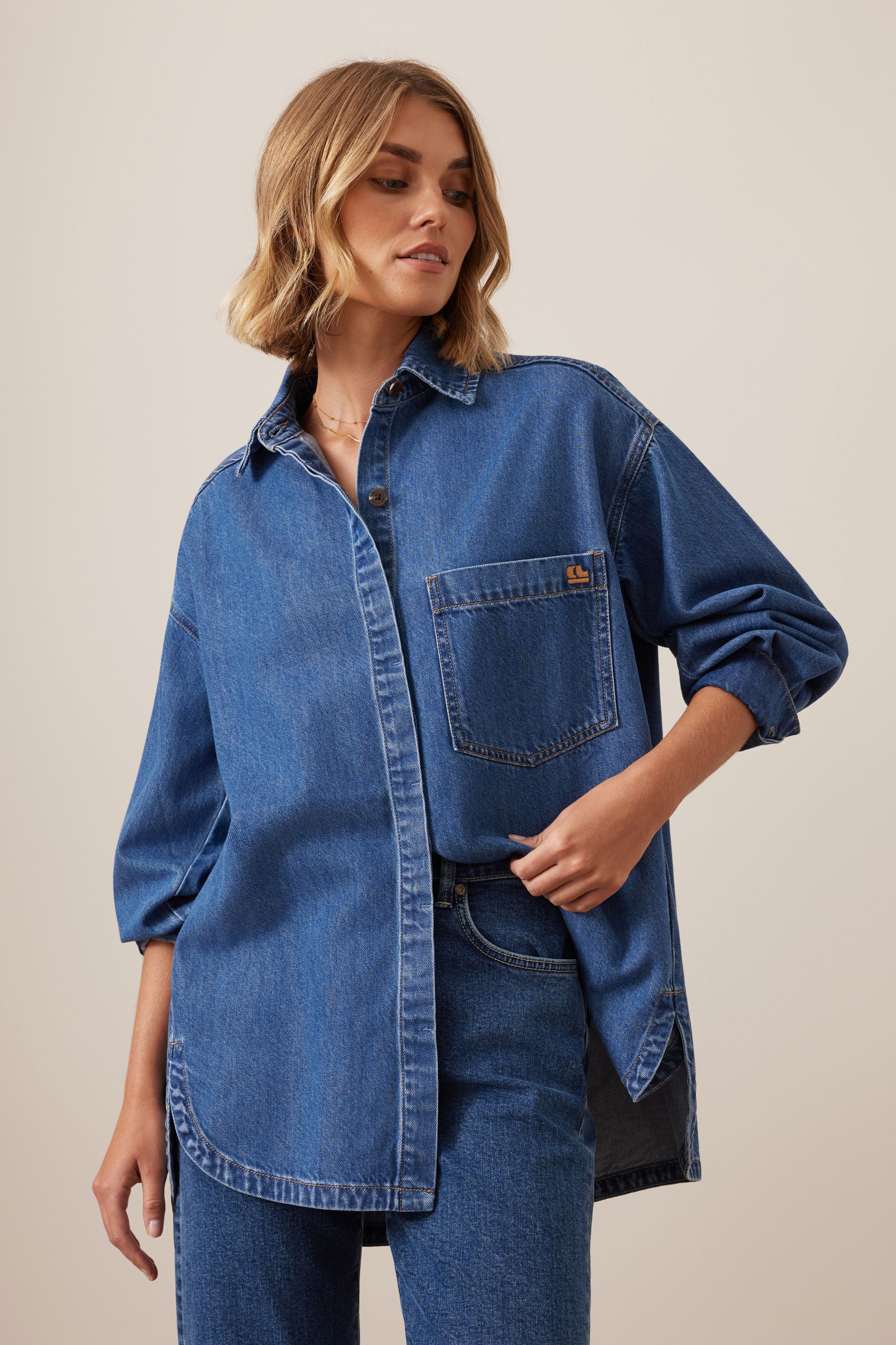 Woman wearing a Ceres Life blue denim shirt and jeans on a beige background