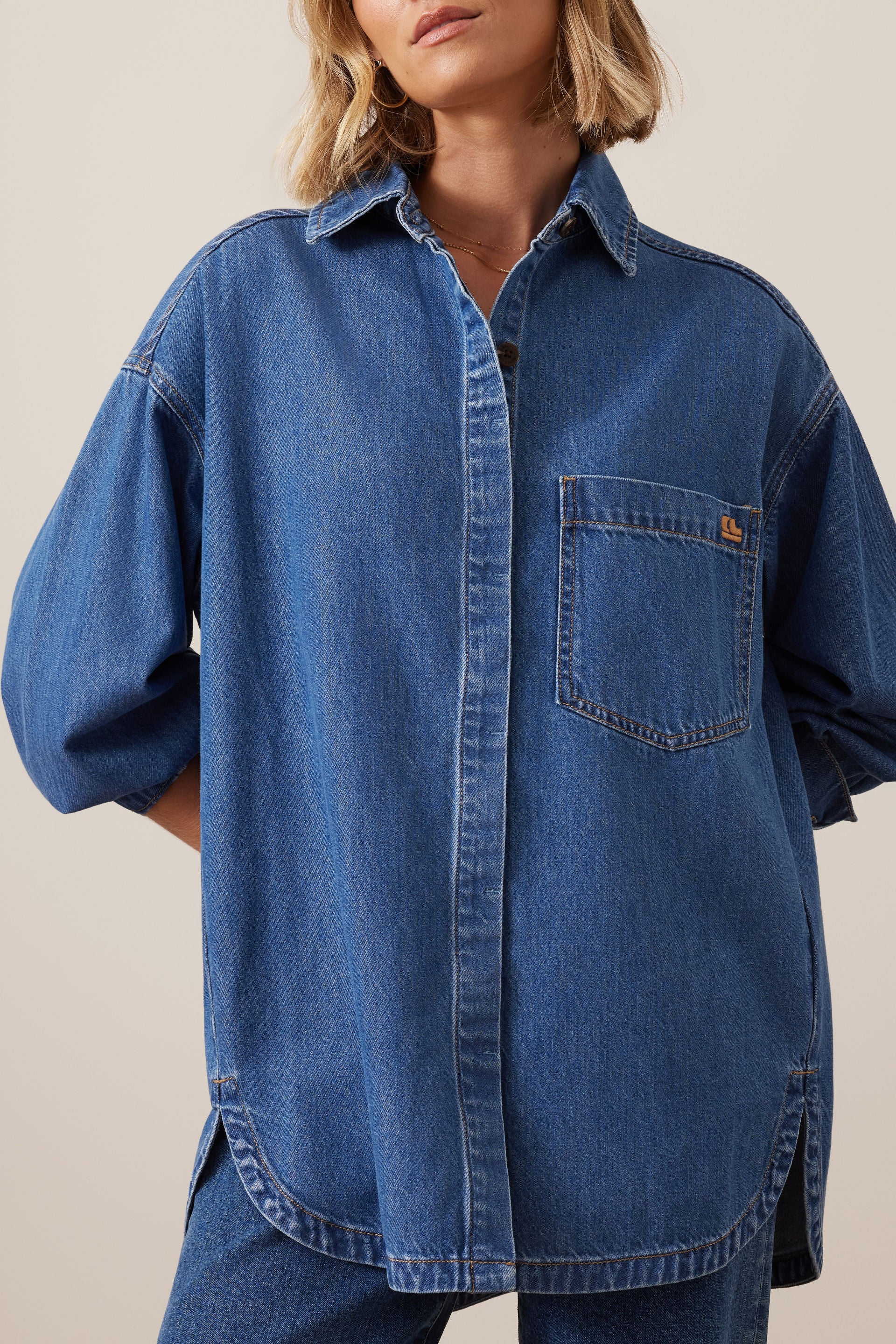 Ceres Life blue denim shirt worn by a woman on a beige background
