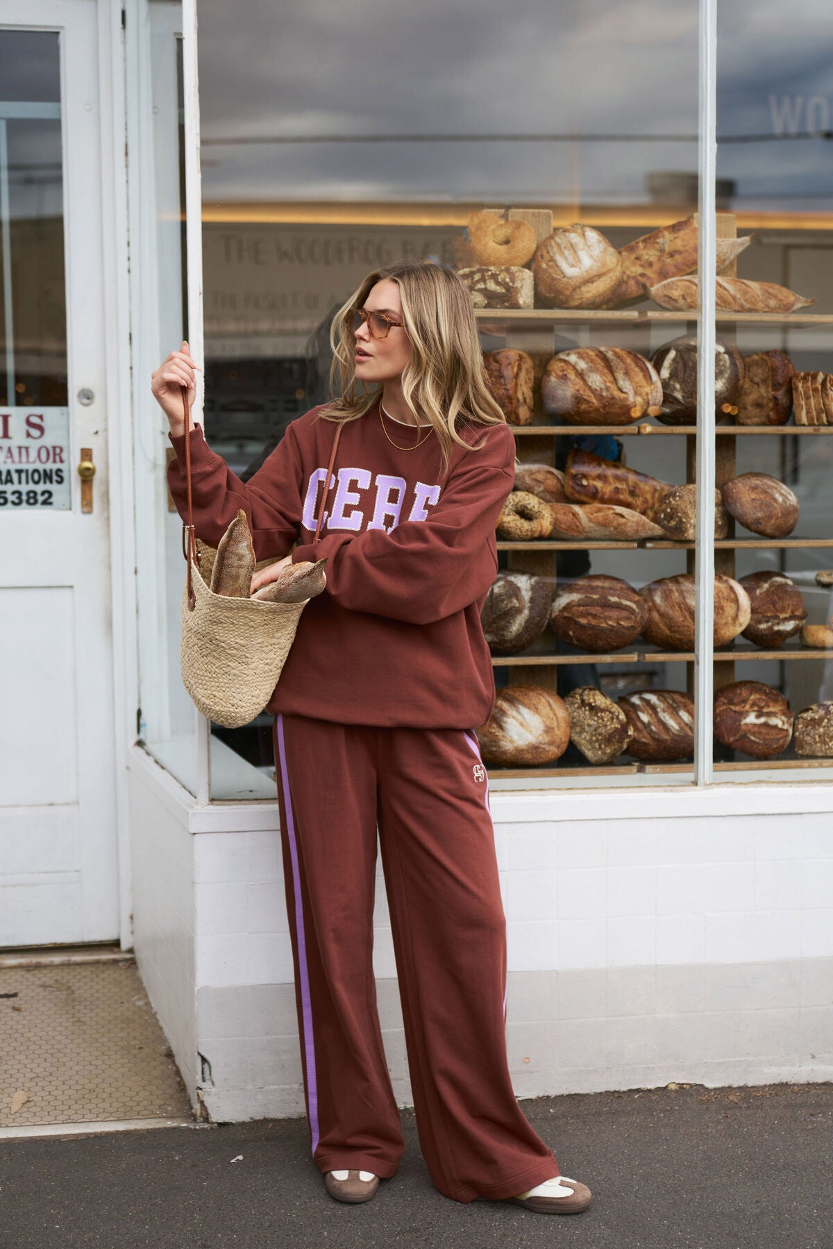 Image of Woman in Ceres maroon tracksuit standing outside a bakery with bread displayed in the window.
