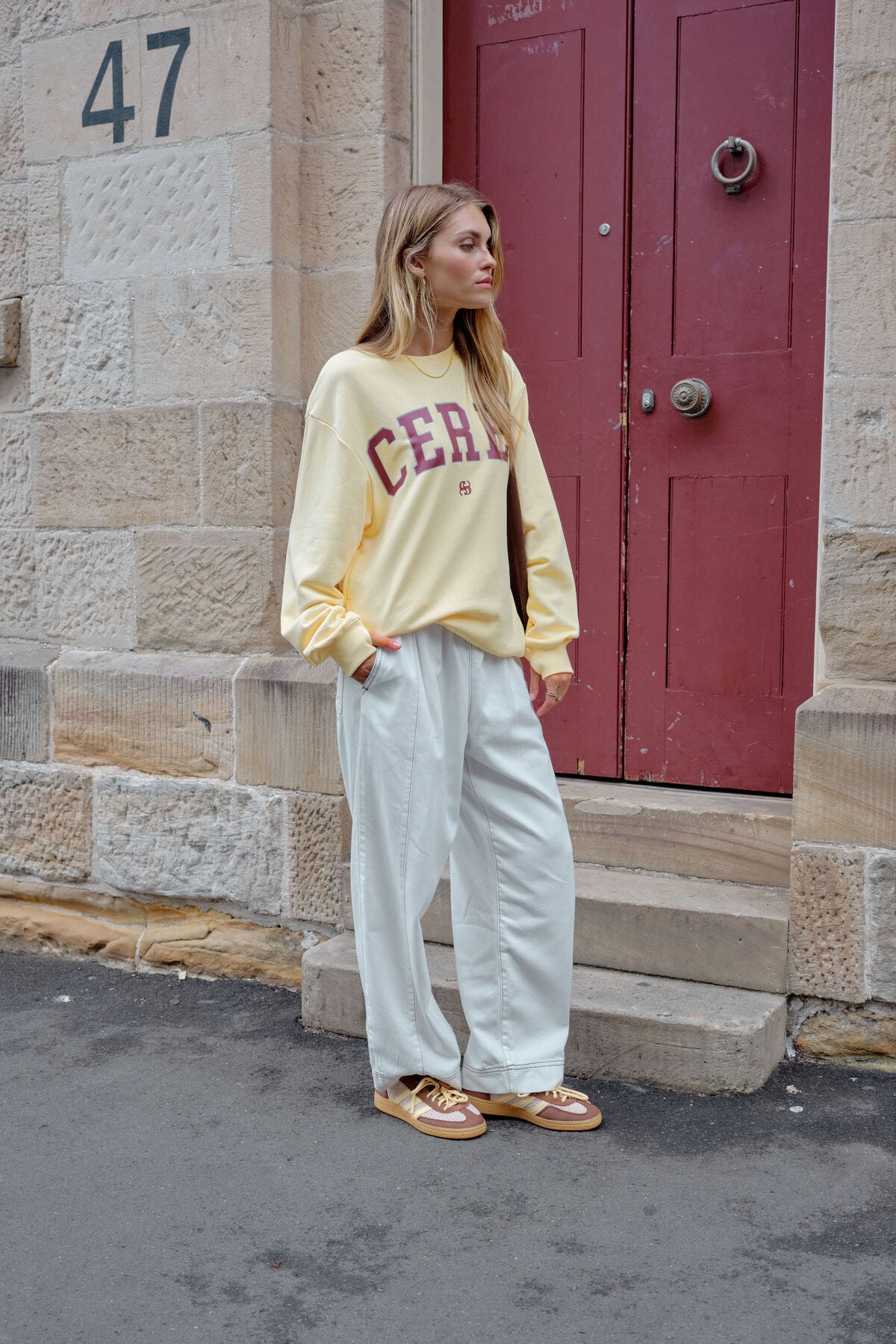 Image of Woman wearing a yellow sweatshirt with 'CERES' printed on it, standing in front of a red door.