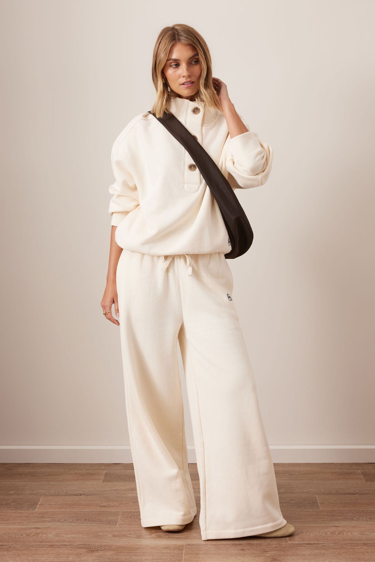 Woman wearing a Ceres Life white outfit with a black bag against a plain background