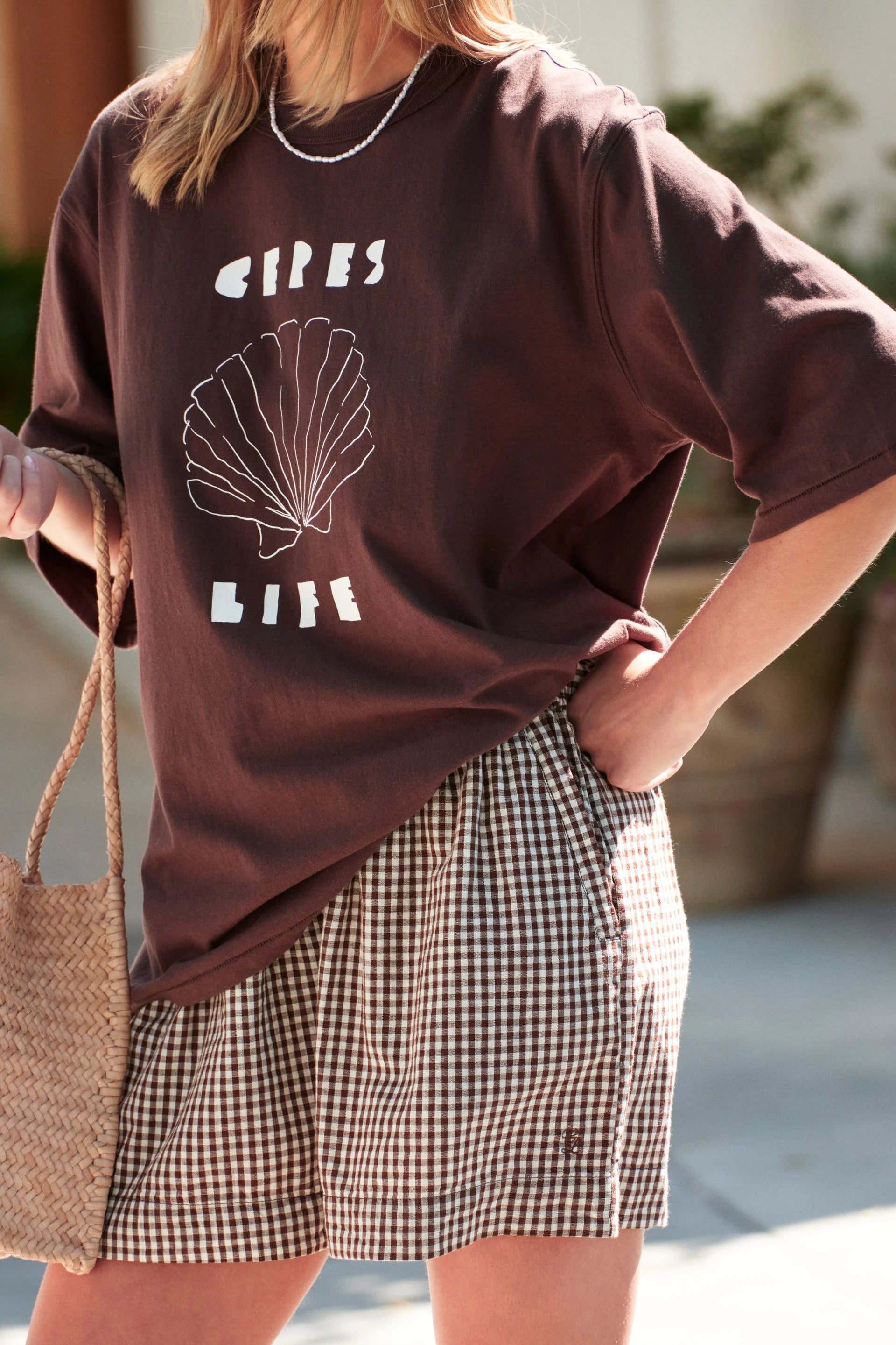 Image of Woman wearing Brown Ceres t shirt paired with checkered shorts 