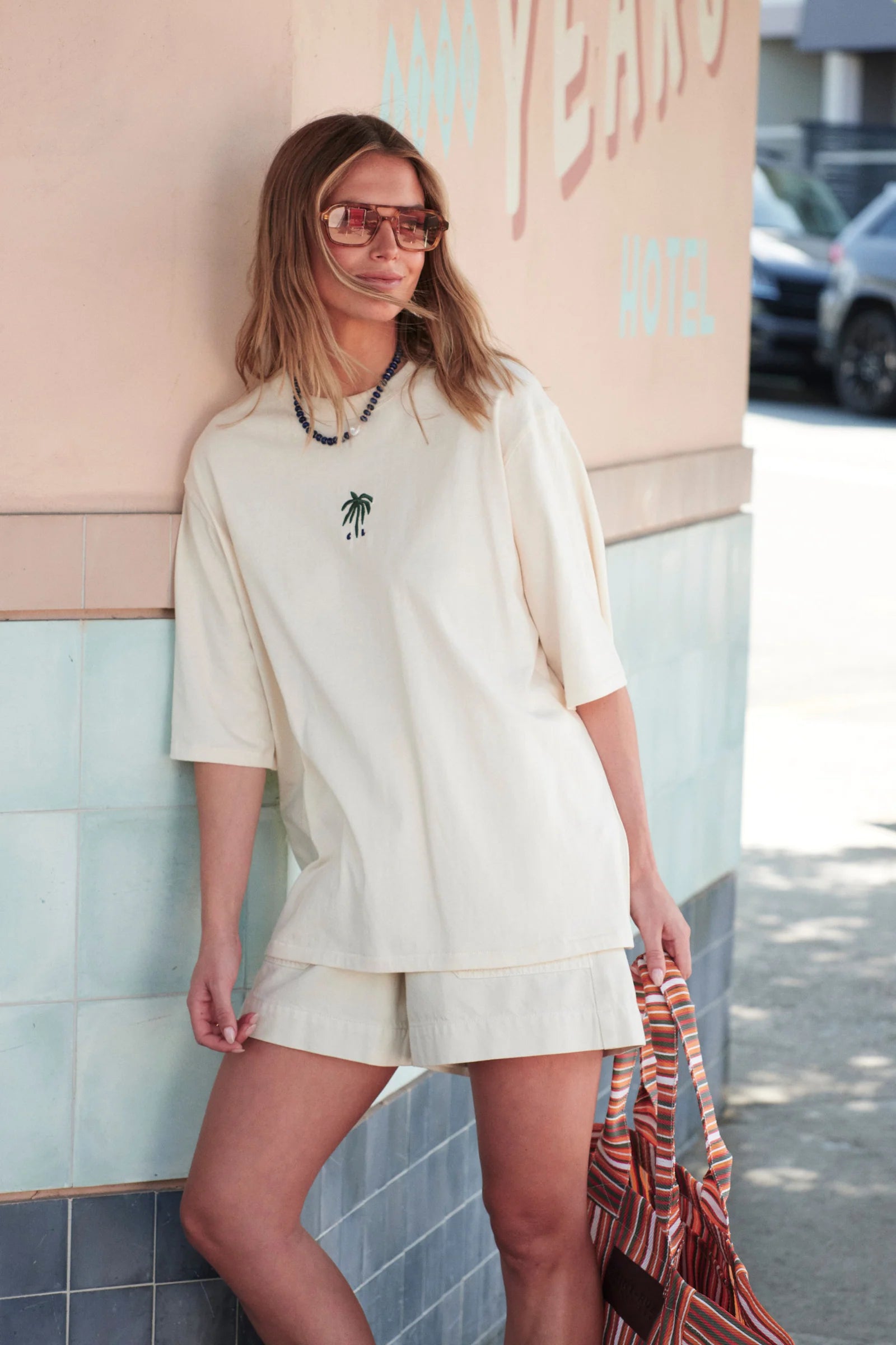 Image of Woman wearing white Ceres tshirt with a palm tree embroidered on the front paired with white shorts. 