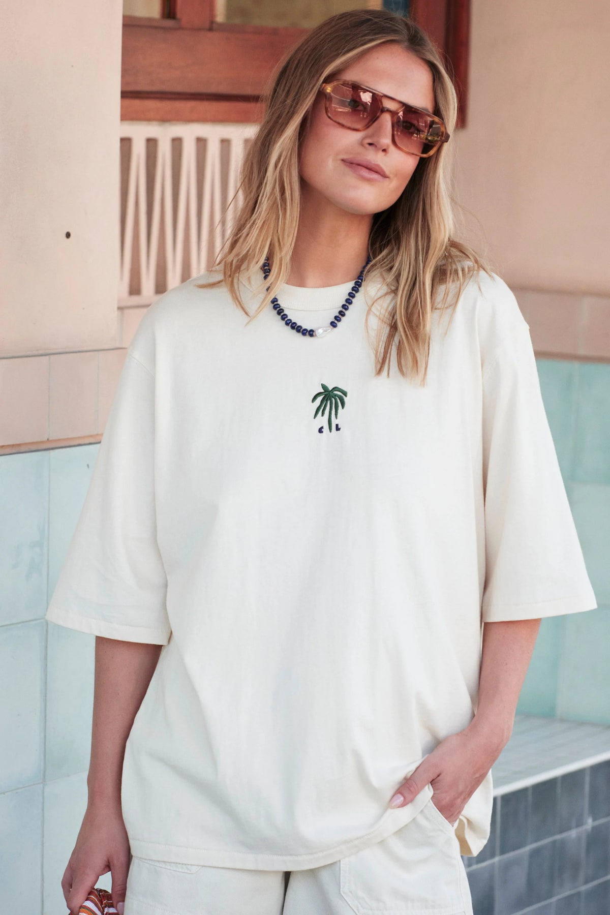 Woman wearing white Ceres tshirt with a palm tree embroidered on the front paired with white shorts. 
