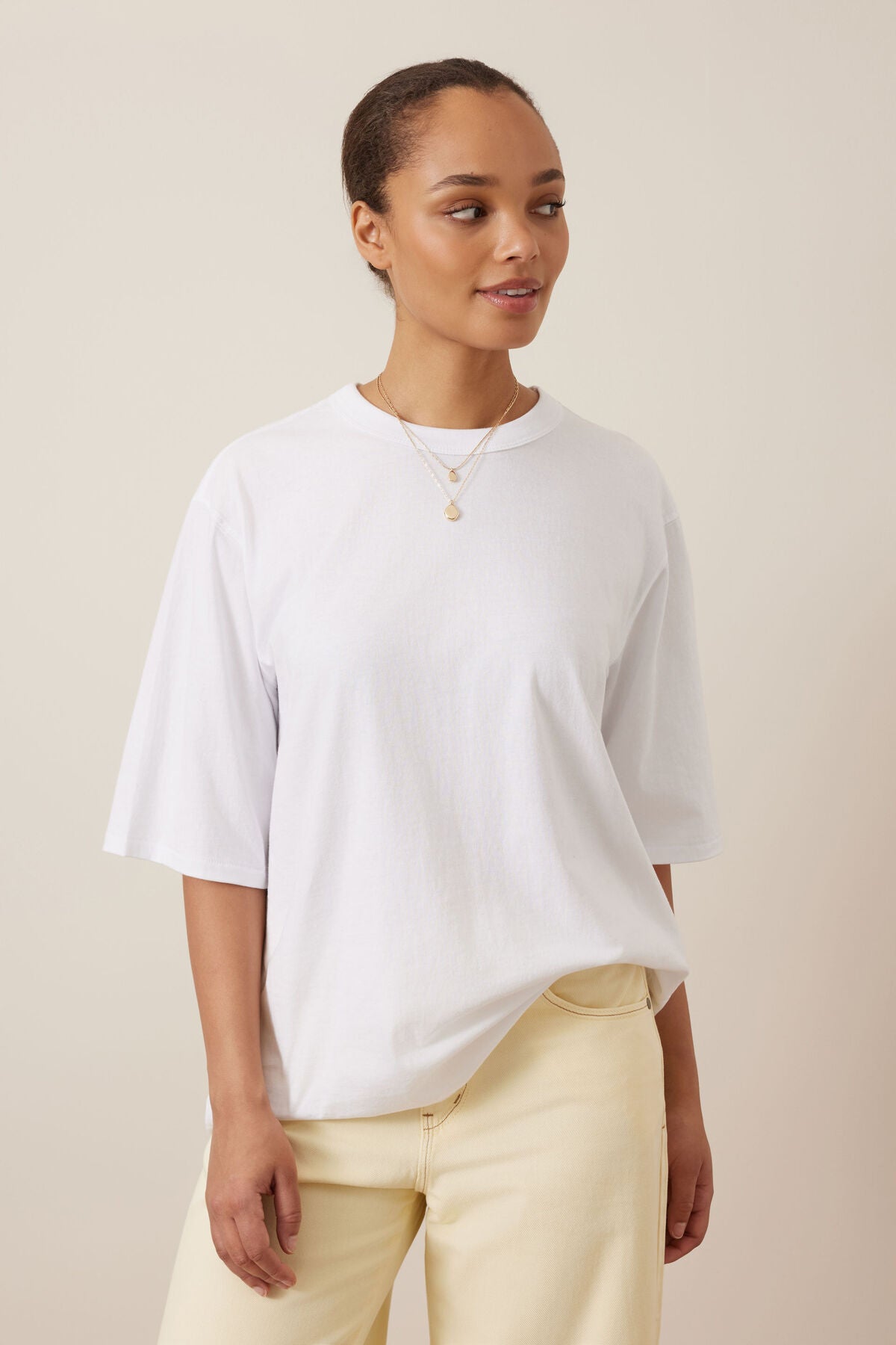 Image of A woman wearing a Ceres Life white oversized short-sleeve crewneck t-shirt and cream-colored pants, standing against a solid beige background.