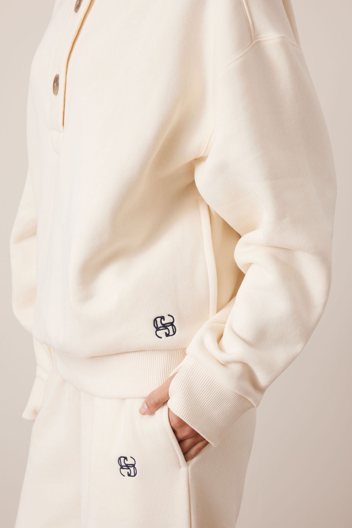 Image of Close-up of a woman wearing a Ceres Life cream-colored outfit with a brand logo on a neutral background