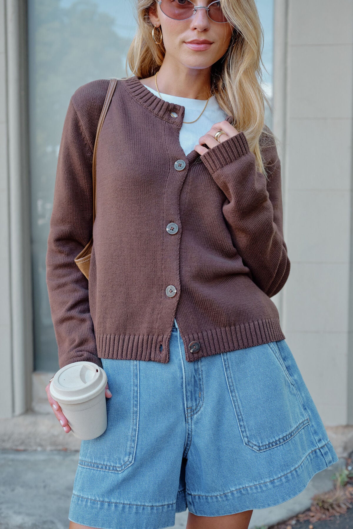 Image of Woman wearing a Ceres Life brown cardigan and blue shorts, holding a coffee cup.