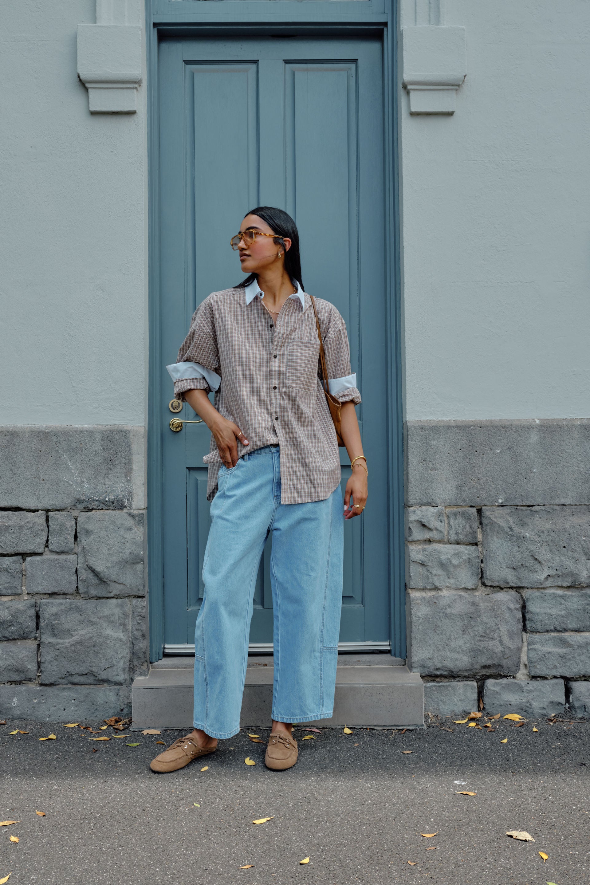 Image of Woman standing in front of a blue door wearing a Ceres checkered shirt and light blue jeans.