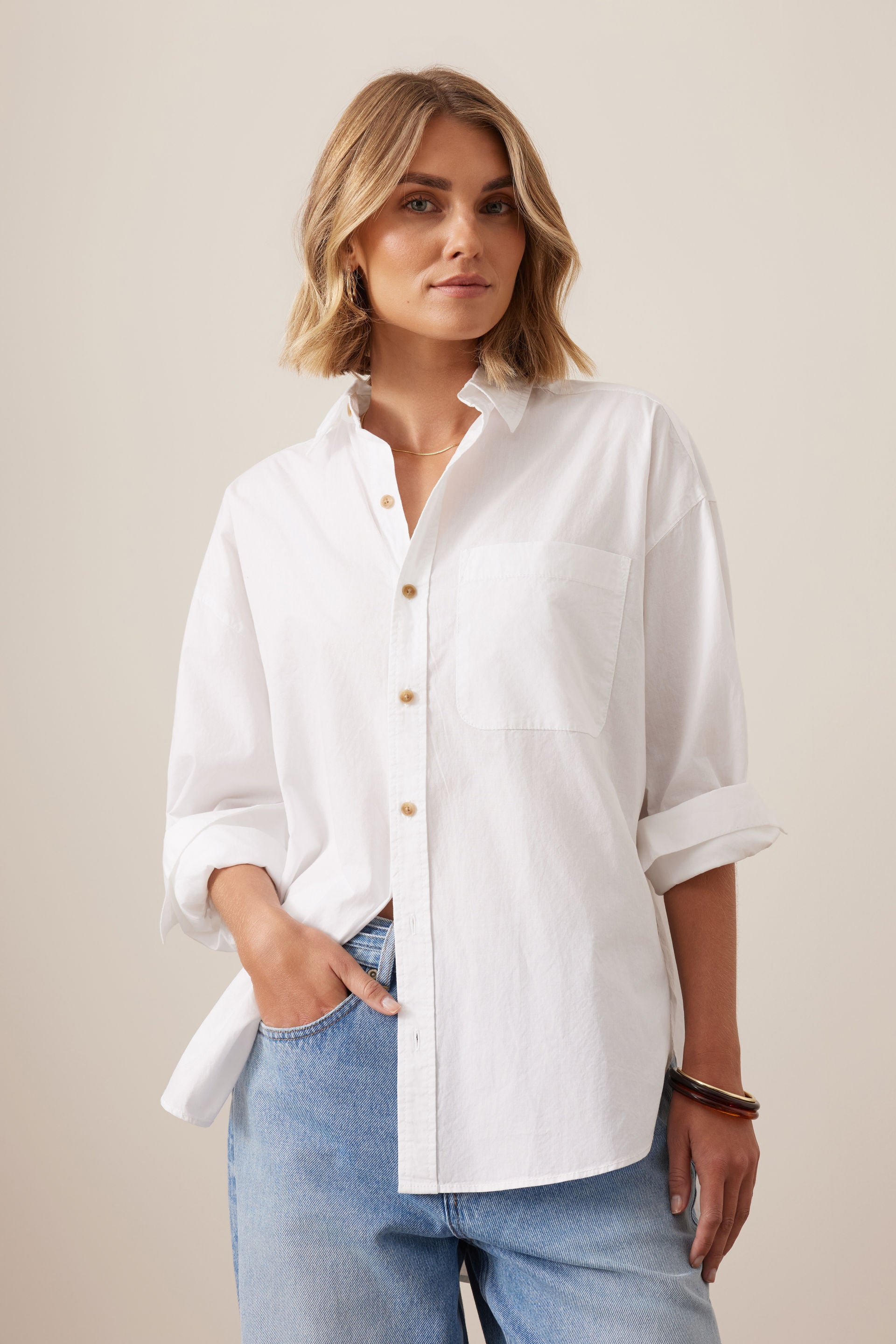 Image of Woman wearing a Ceres Life white shirt and blue jeans against a beige background