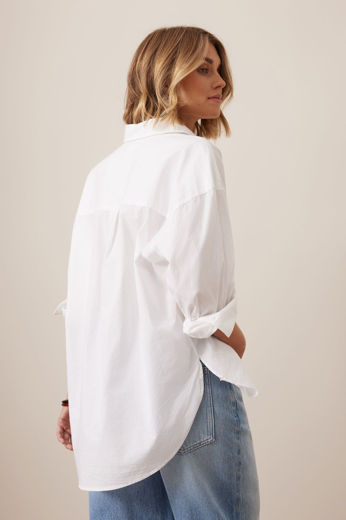 Woman wearing a Ceres Life white oversized shirt and blue jeans against a beige background
