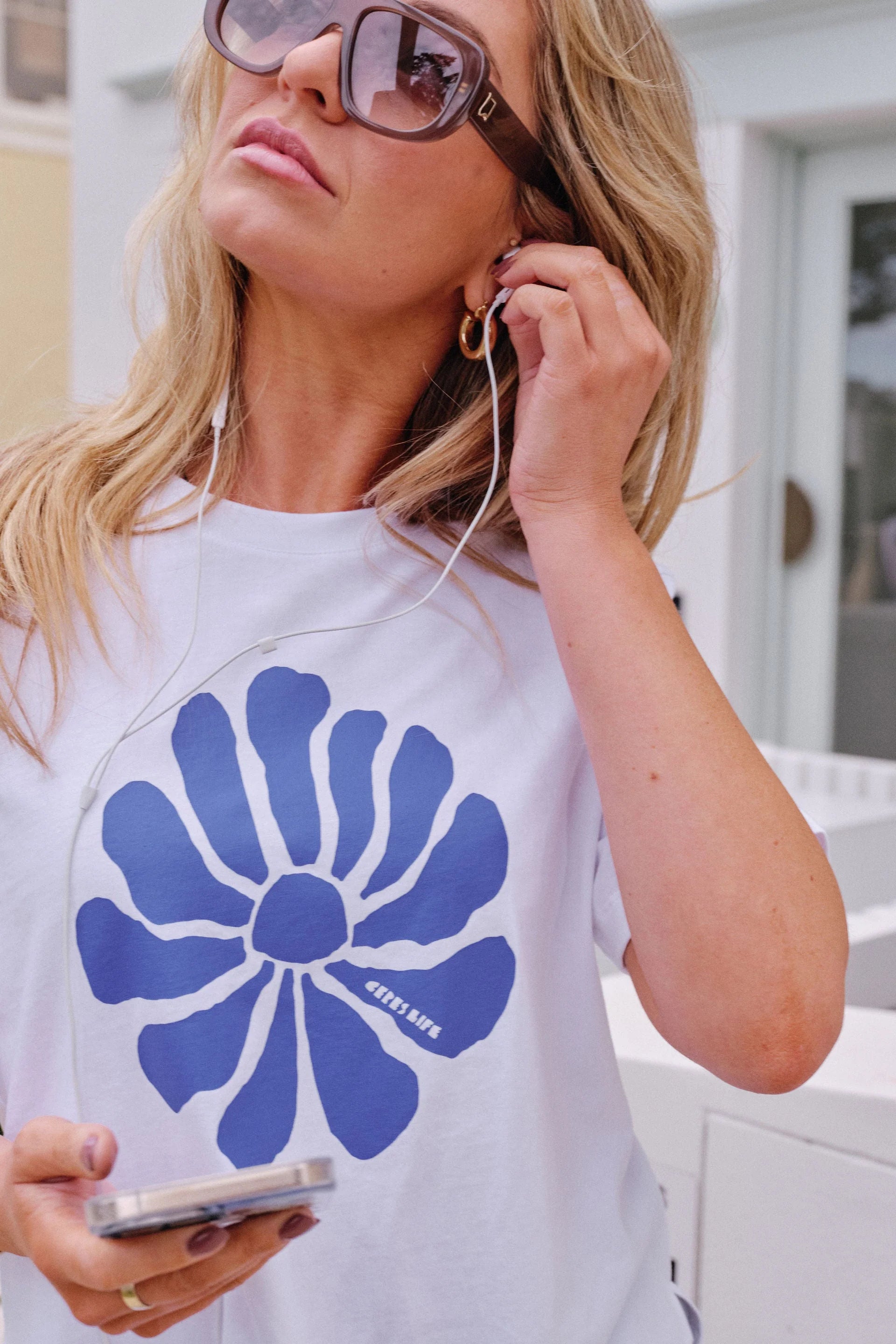Image of Woman wearing Ceres Life, white tshirt with a feature flower on the front paired with khaki trousers and thongs