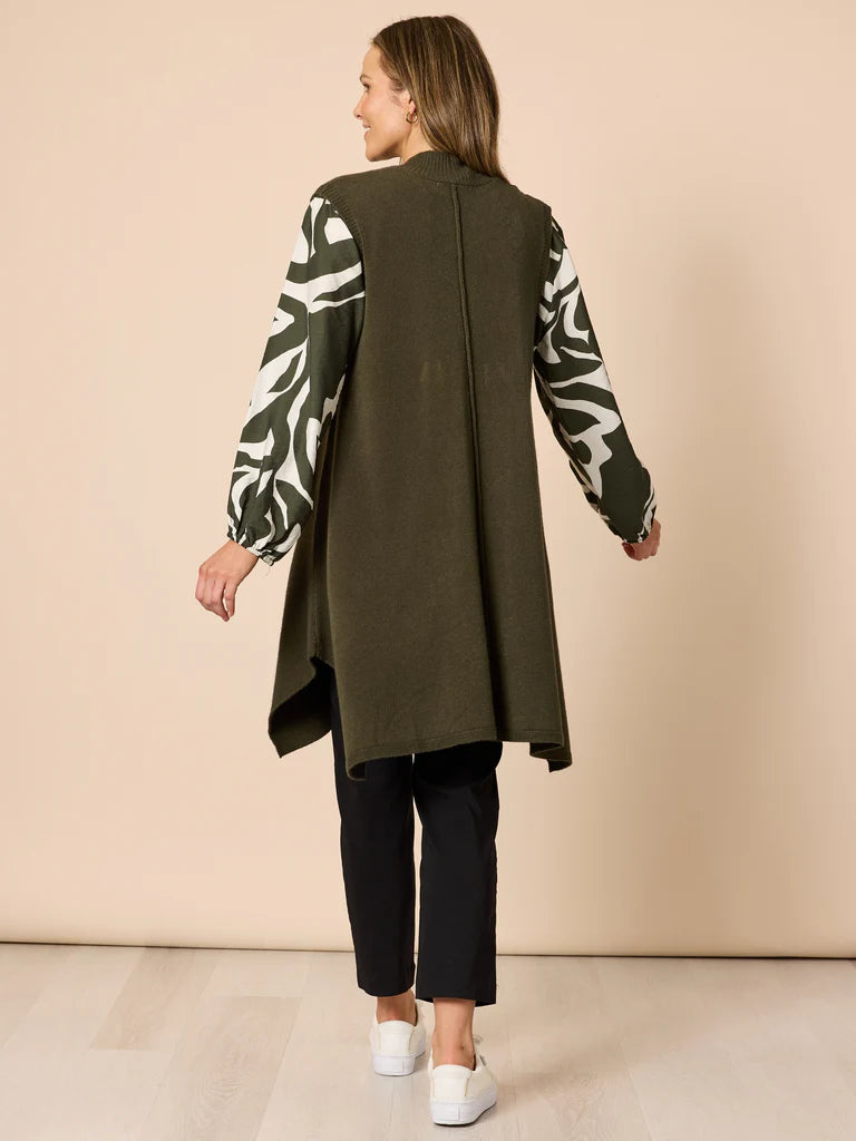 Woman wearing a Clarity long green coat over a patterned top with black pants against a beige background