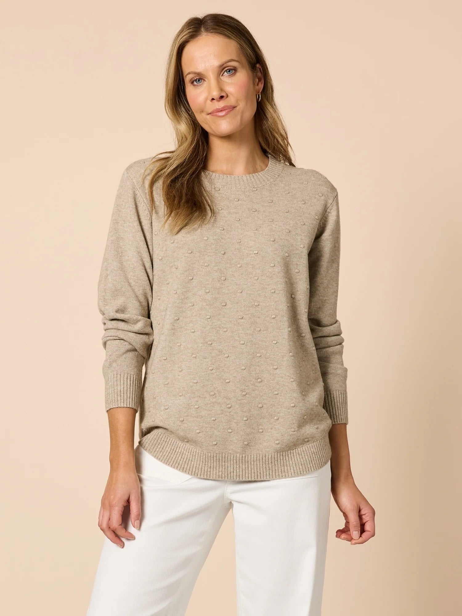 Woman wearing a Clarity beige sweater and white pants on a beige background