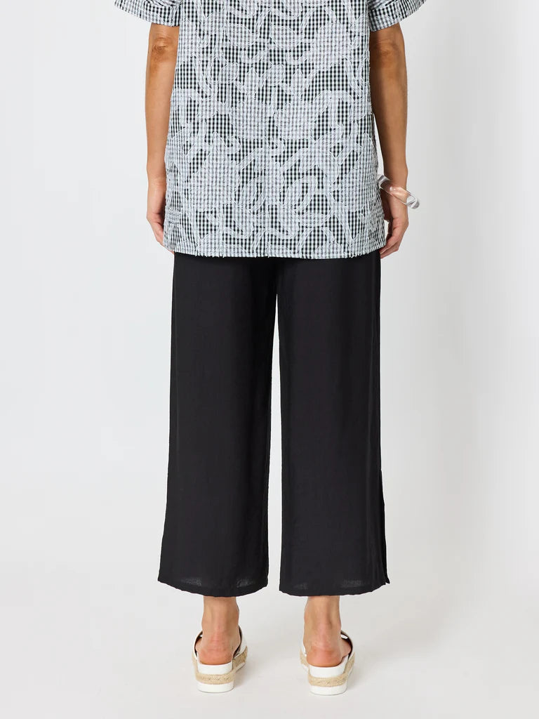 A model from the back wearing a Clarity black wide-leg cropped trouser, a black and white patterned short-sleeve top, and white platform sandals against a light gray studio background.