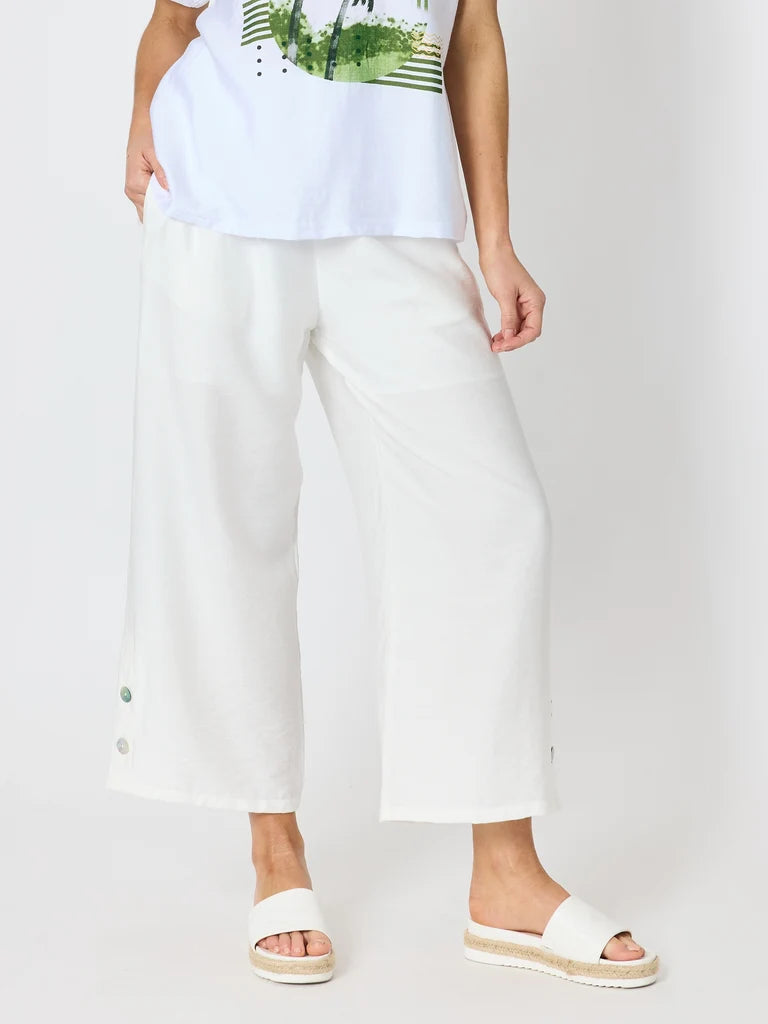 Woman wearing Clarity white cropped wide-leg pants with a white graphic T-shirt and white slide sandals, photographed against a light gray studio background.