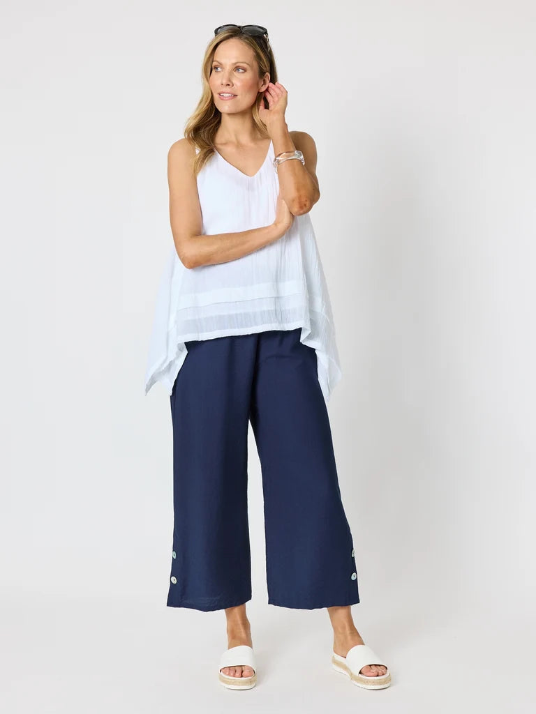 Image of A woman modeling a Clarity white sleeveless top and navy blue wide-leg cropped pants with white slide sandals, photographed against a light grey studio background.