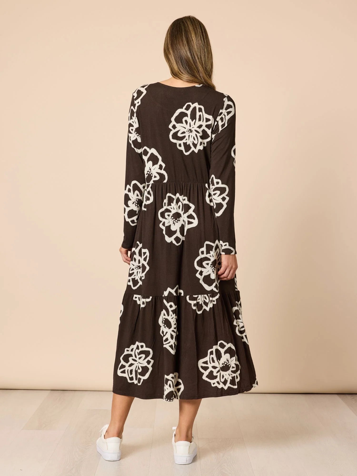 Woman wearing a Clarity brown dress with white floral patterns against a beige background
