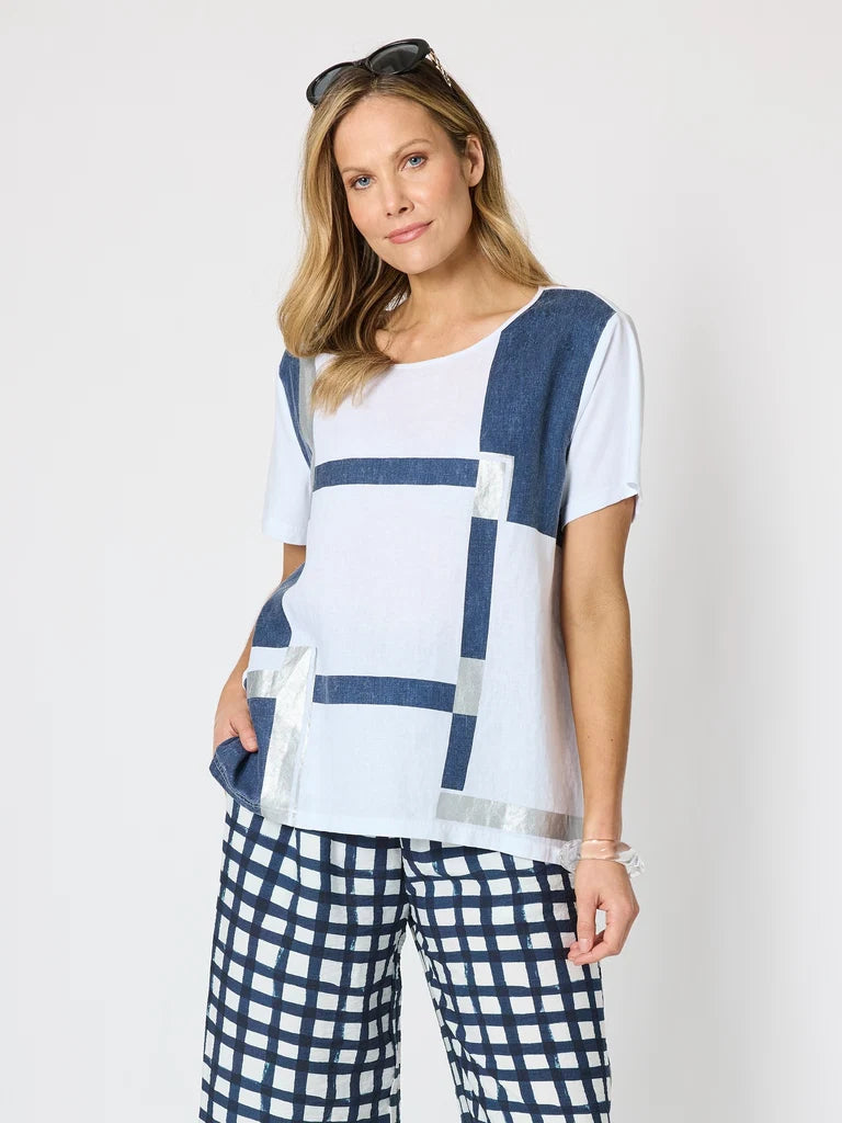 Image of A woman modeling a Clarity white short-sleeve top with navy blue geometric block patterns and matching navy and white checkered pants, photographed against a plain light gray studio background.