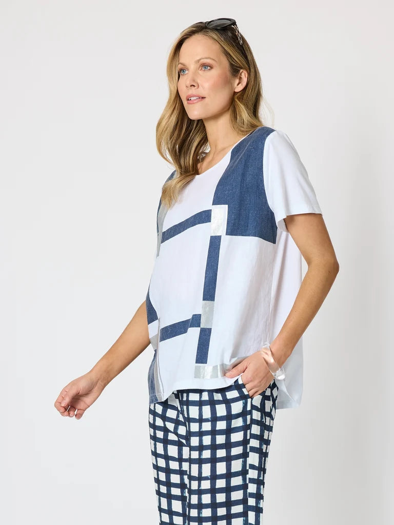 Image of A woman modeling a Clarity white short-sleeve top with a blue geometric block pattern, paired with blue and white checkered pants, against a plain light gray background.