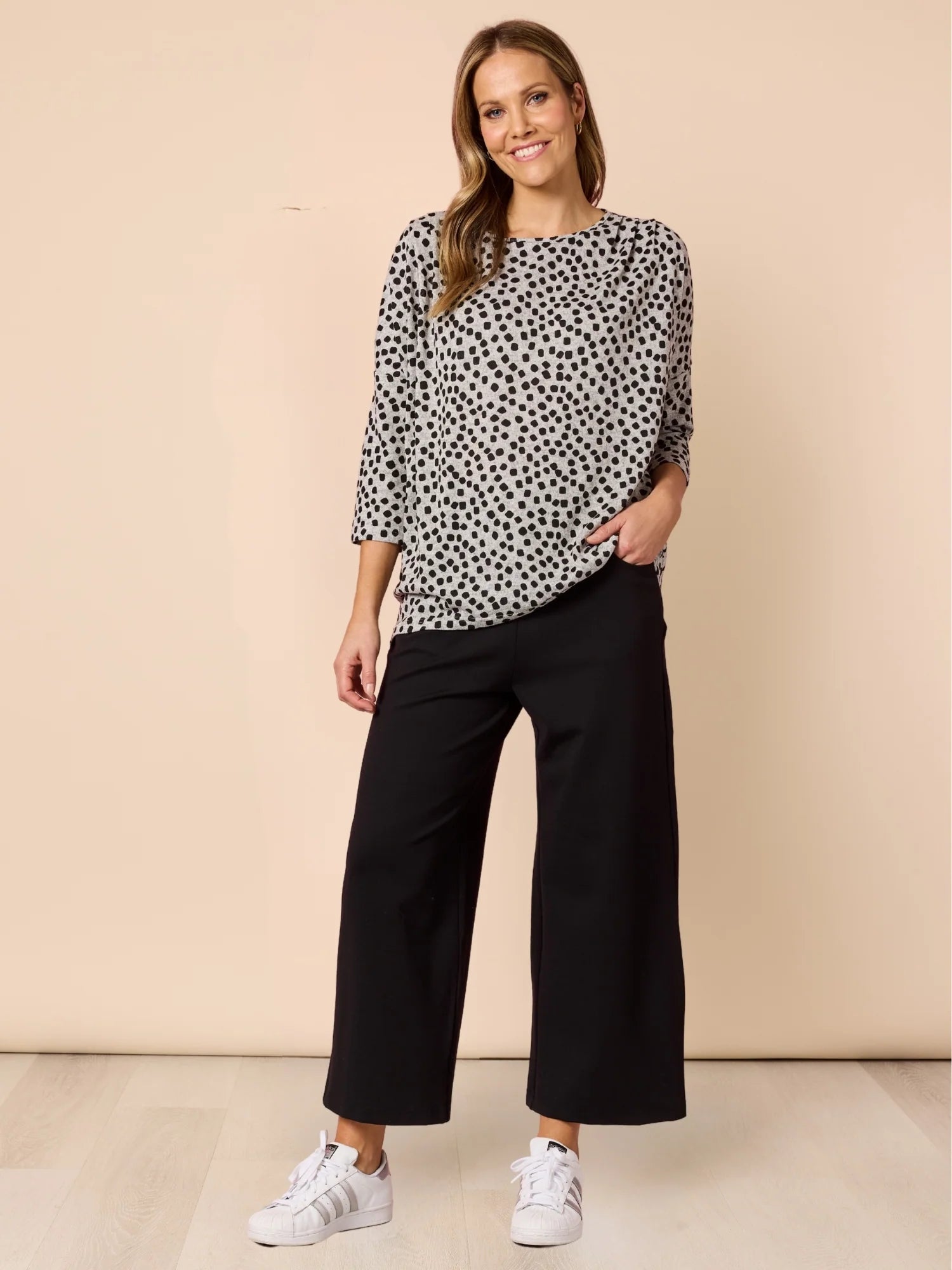 Image of Woman wearing a patterned top and Clarity black pants against a beige background