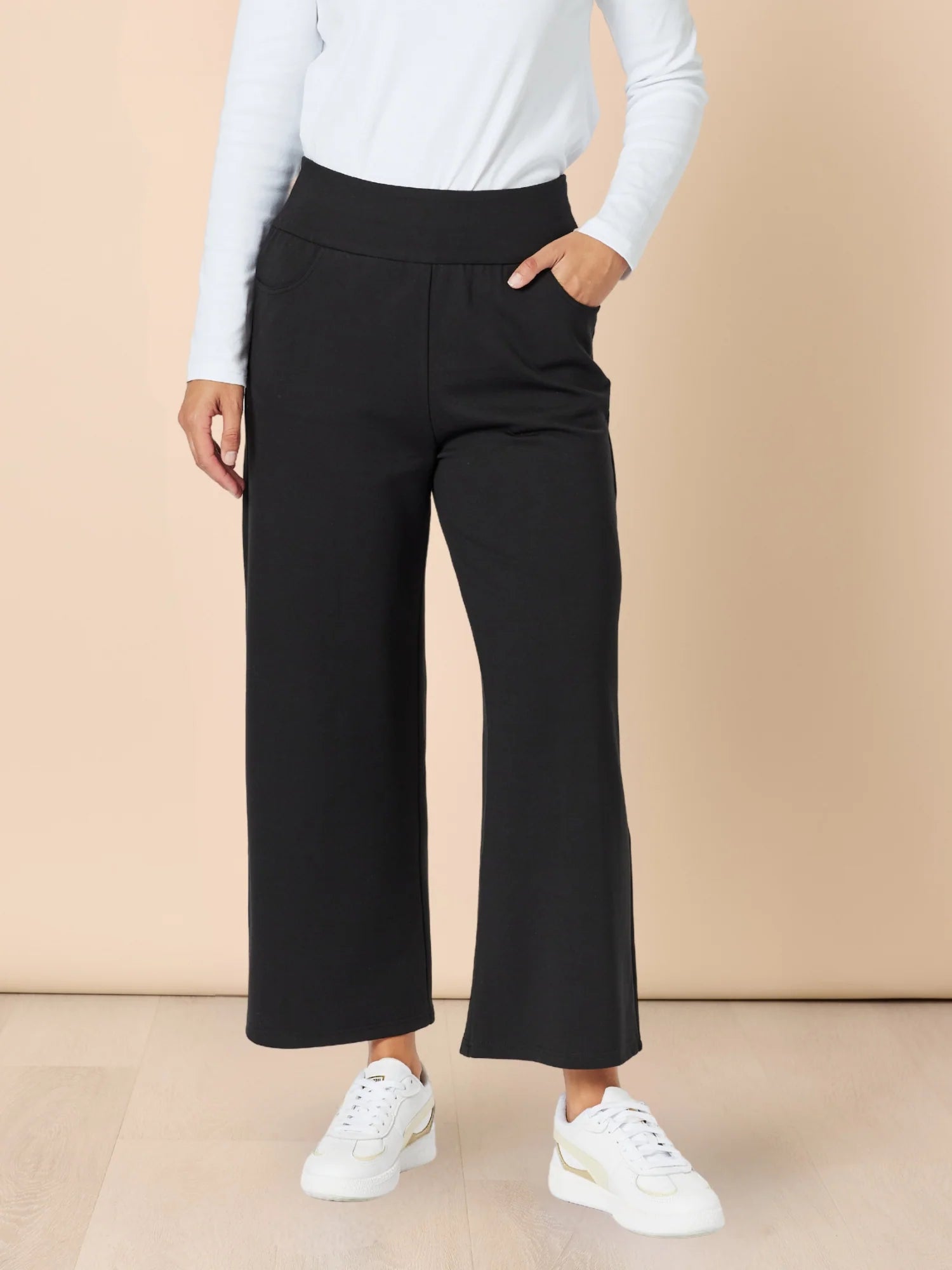 Image of Woman wearing black wide-leg pants and white sneakers on a beige background