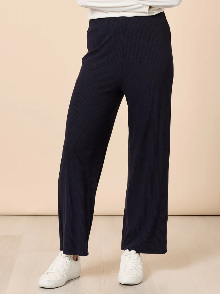 Image of Person wearing Clarity navy pants and white sneakers on a beige background