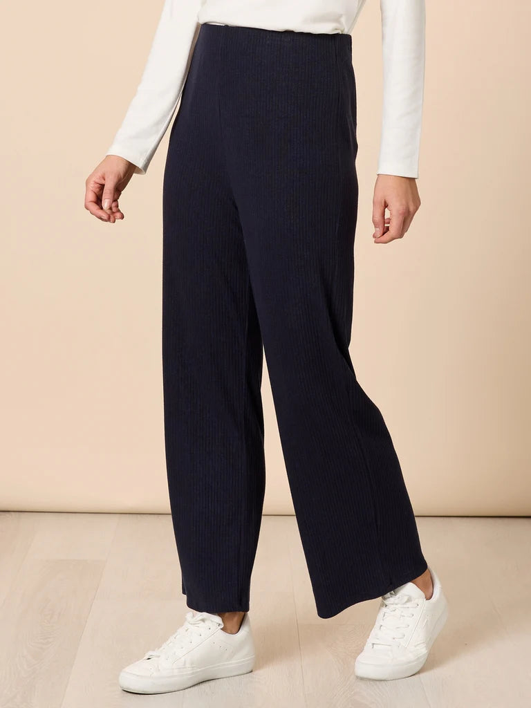 Image of Person wearing Clarity navy ribbed pants with a white top and white sneakers on a beige background