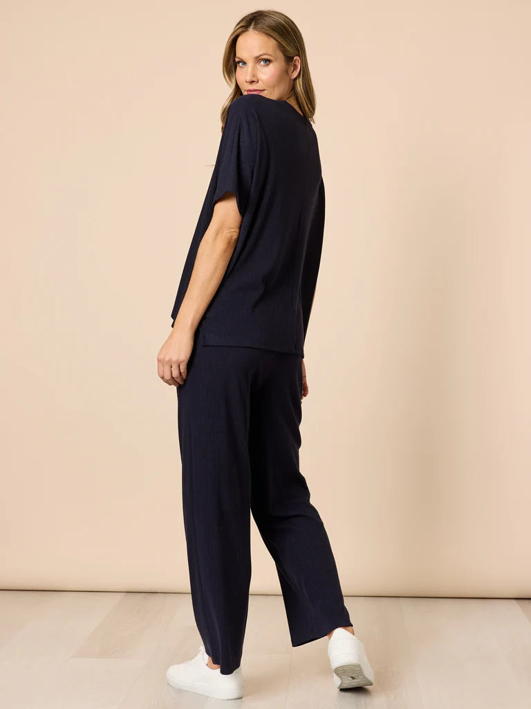 Woman wearing Clarity navy outfit with white shoes on a beige background