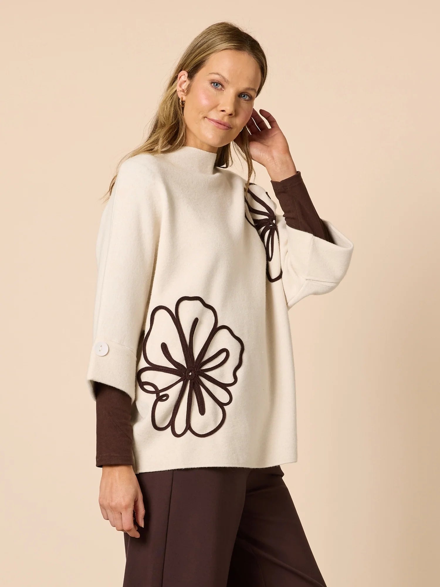 Woman wearing a Clarity cream-colored poncho with a black floral design on a beige background