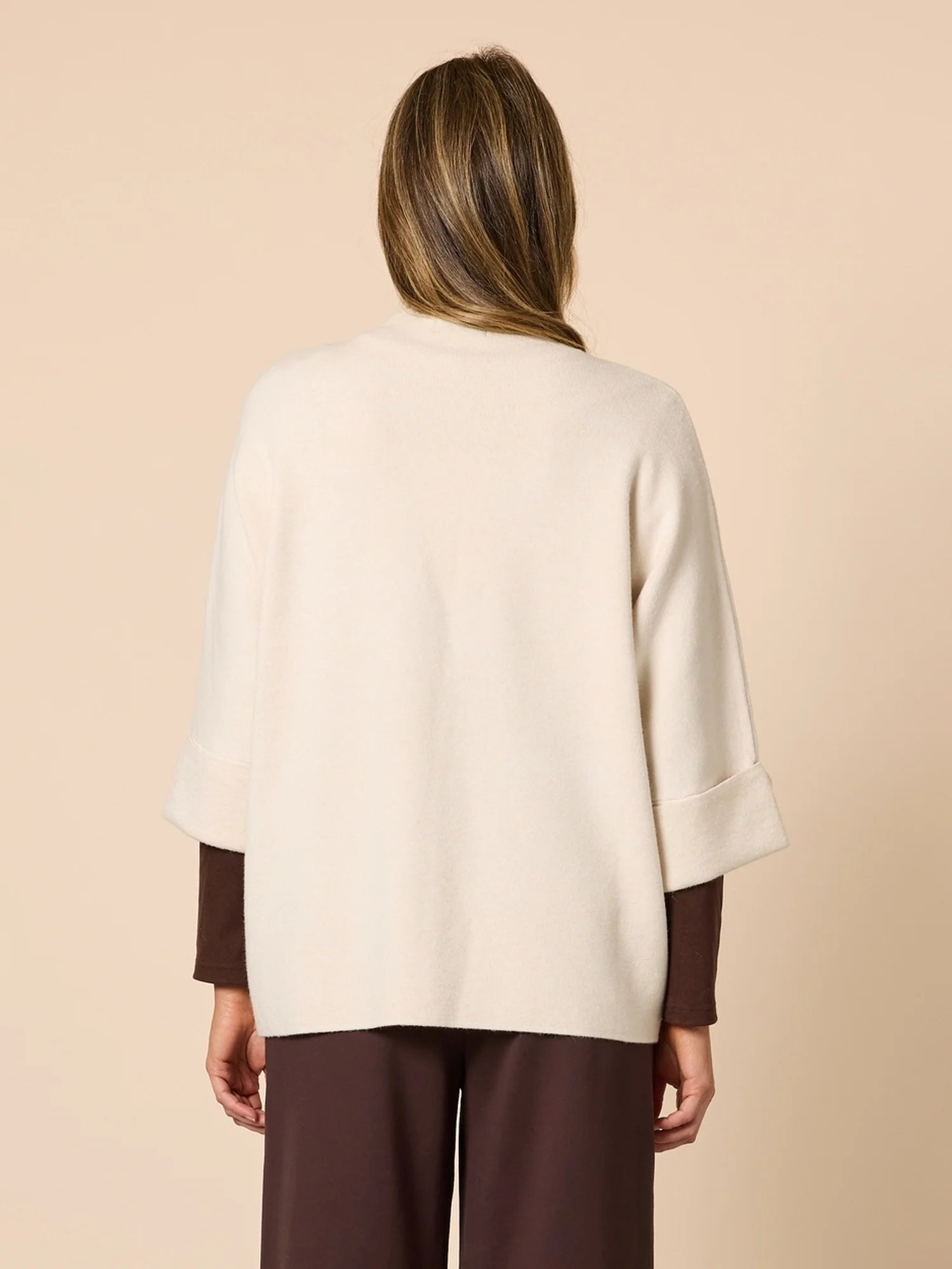 Woman wearing a Clarity cream-colored cardigan with brown cuffs and hem on a beige background