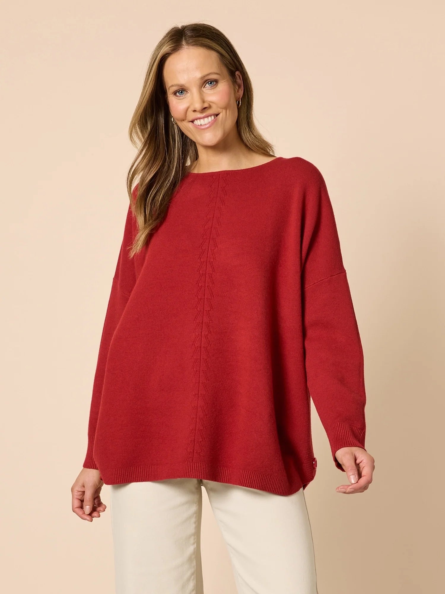 Woman wearing a Clarity red sweater and white pants on a beige background