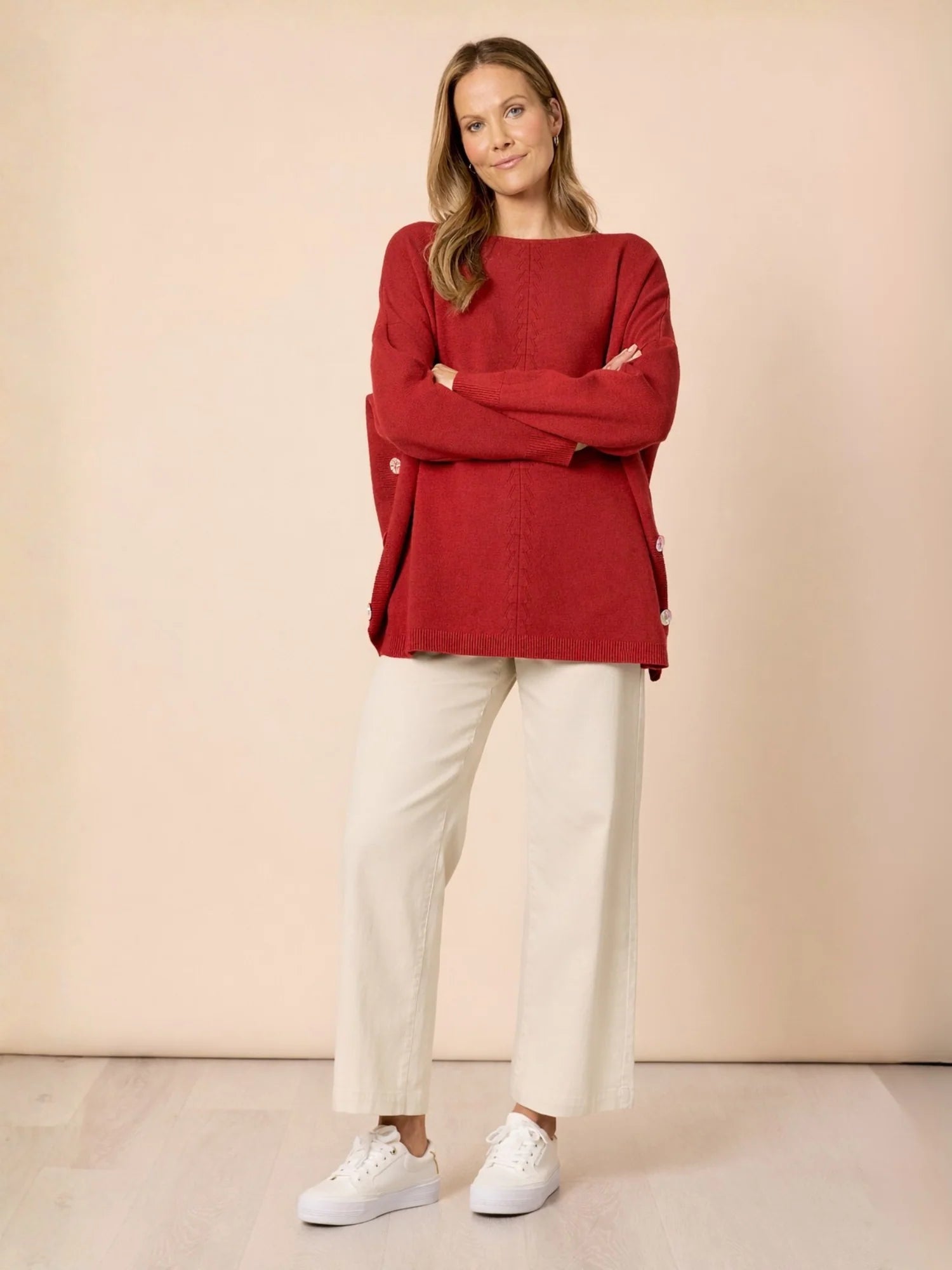 Image of Woman wearing a Clarity red sweater and white pants against a beige background