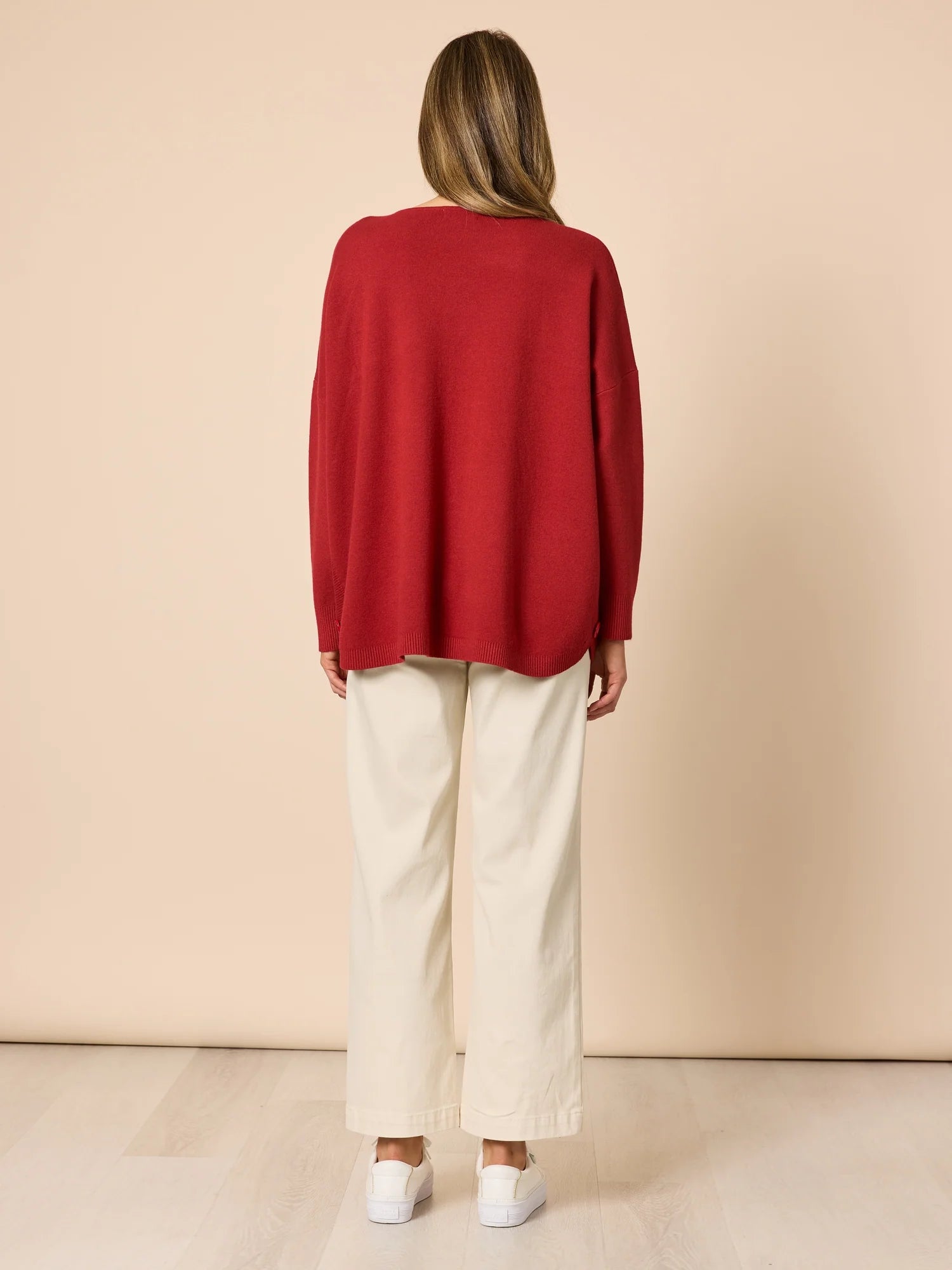 Woman wearing a Clarity red sweater and white pants against a beige background