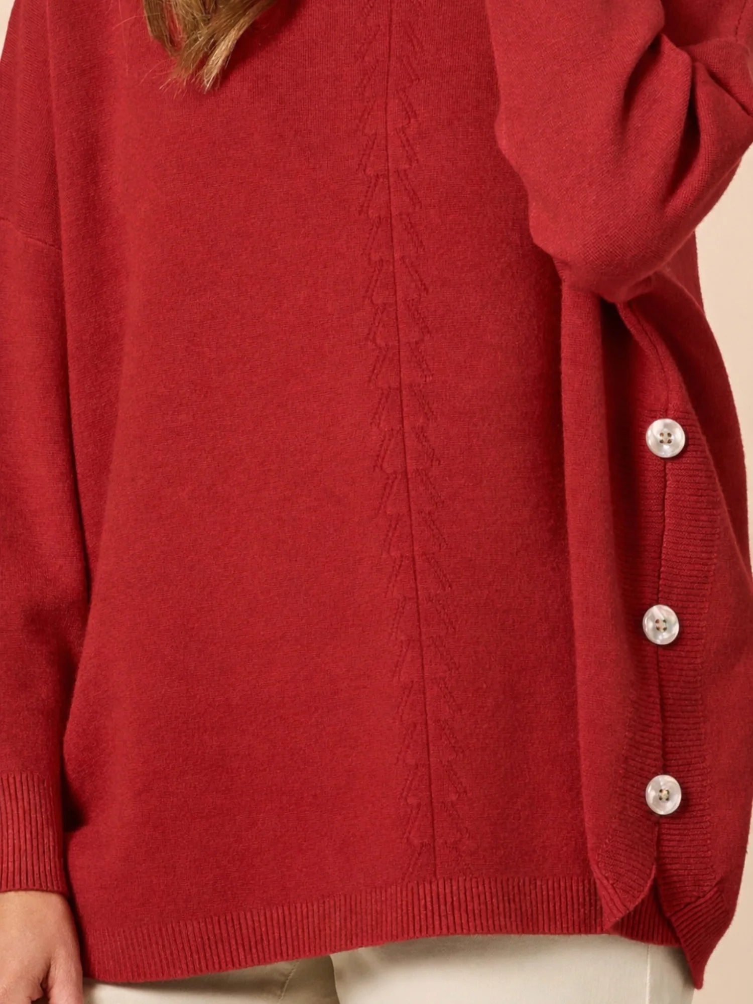 Image of Close-up of a Clarity red cardigan with silver buttons on a beige background