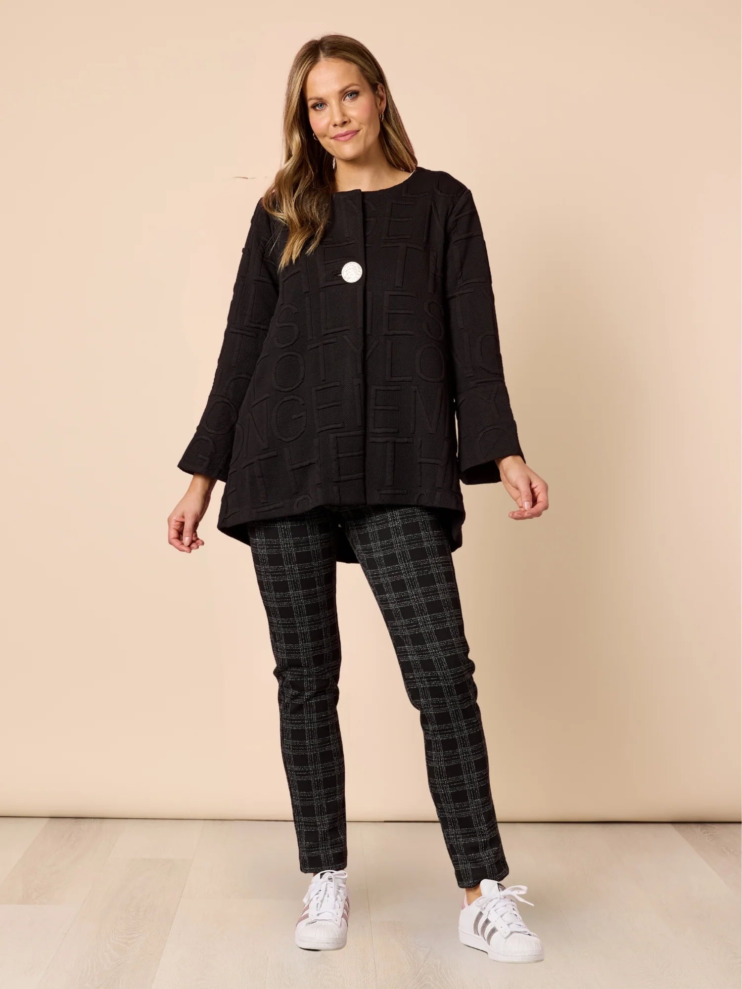 Image of Woman wearing a Clarity black jacket and plaid pants on a beige background