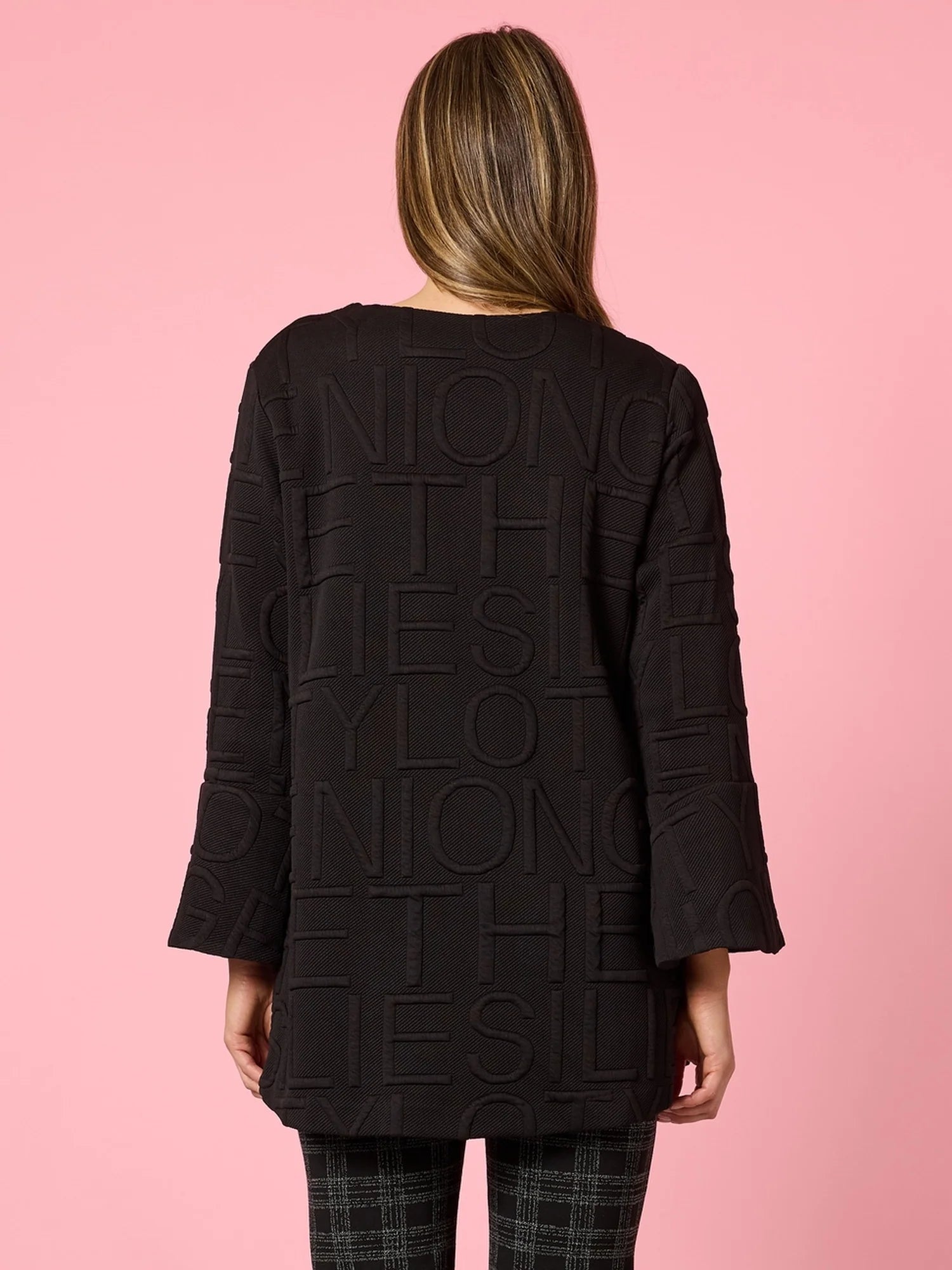 Image of Clarity black textured sweater with text on the back worn by a woman against a pink background