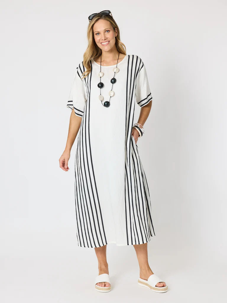 Image of A woman modeling a Clarity white midi dress with vertical black stripes on the sleeves and skirt, styled with a chunky black beaded necklace and white slide sandals against a light gray studio background.