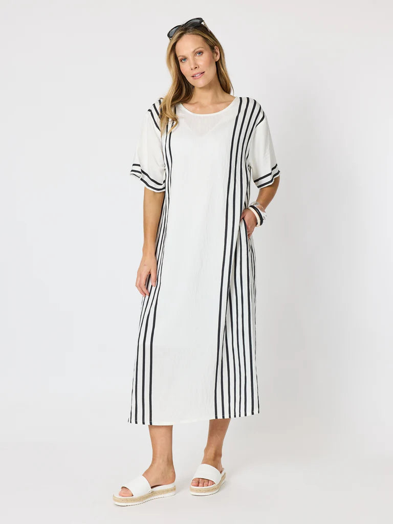 Image of A woman modeling a Clarity white midi dress with black vertical stripes on the sleeves, hem, and side panels, paired with white slide sandals against a plain white studio background.