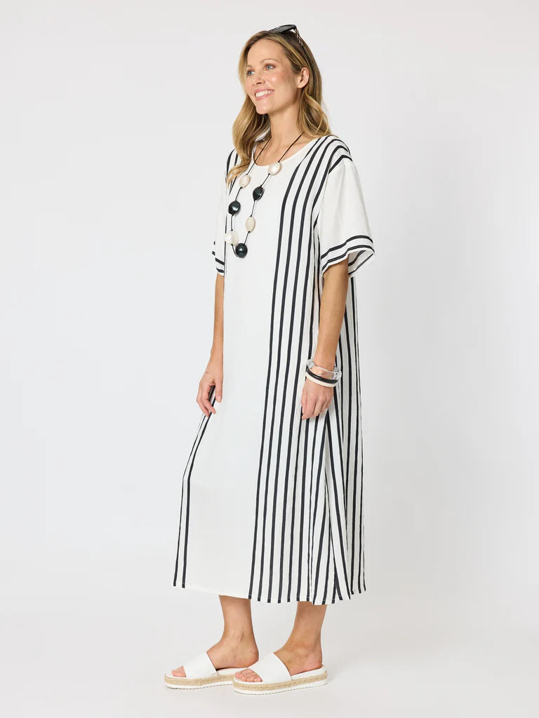 A woman modeling a Clarity white midi dress with vertical black stripes, featuring short sleeves and a round neckline, styled with a long beaded necklace and white slide sandals against a plain white studio background.