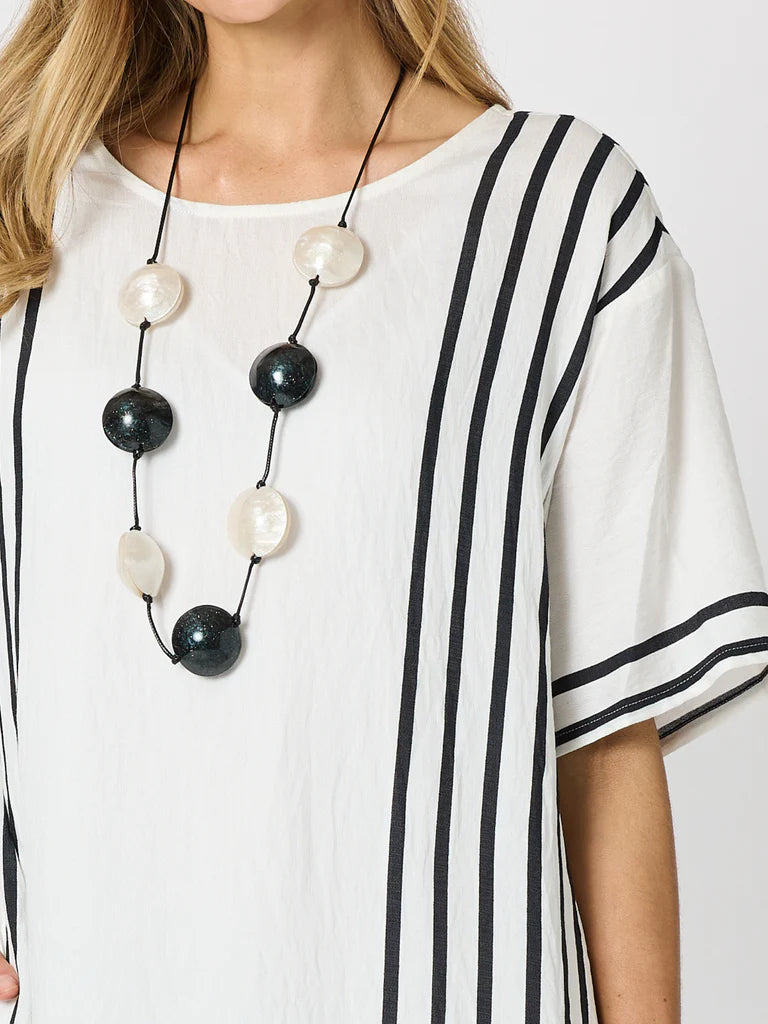 A close-up of a woman wearing a Clarity white short-sleeve top with vertical black stripes and a long black beaded necklace with white and black round beads.