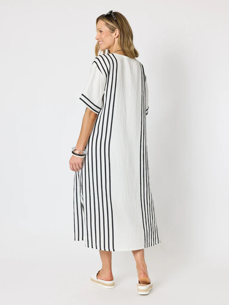 Image of A woman modeling a Clarity white midi dress with vertical black stripes, shown from a rear three-quarter angle against a plain white studio background.