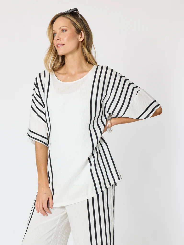 Image of A woman modeling a Clarity white knit top with black vertical stripes on the sleeves and side panels, paired with matching white pants against a light gray studio background.