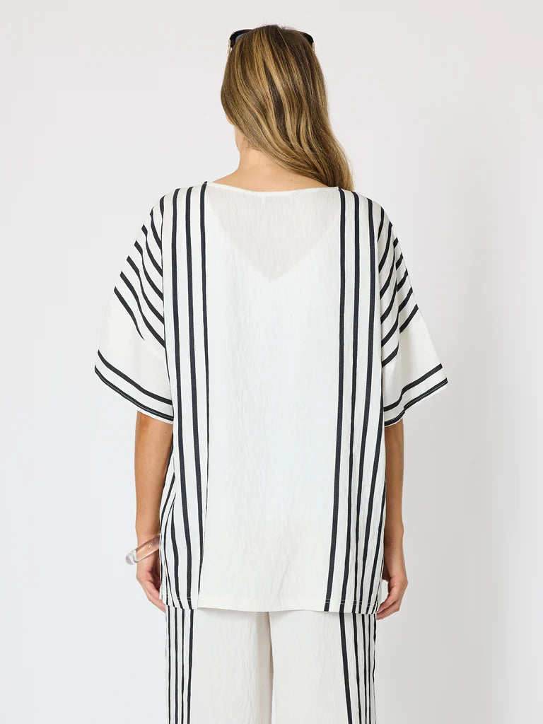 A woman viewed from the back wearing a Clarity loose white top with bold black vertical stripes on the sleeves and sides, paired with matching striped pants, against a plain light background.