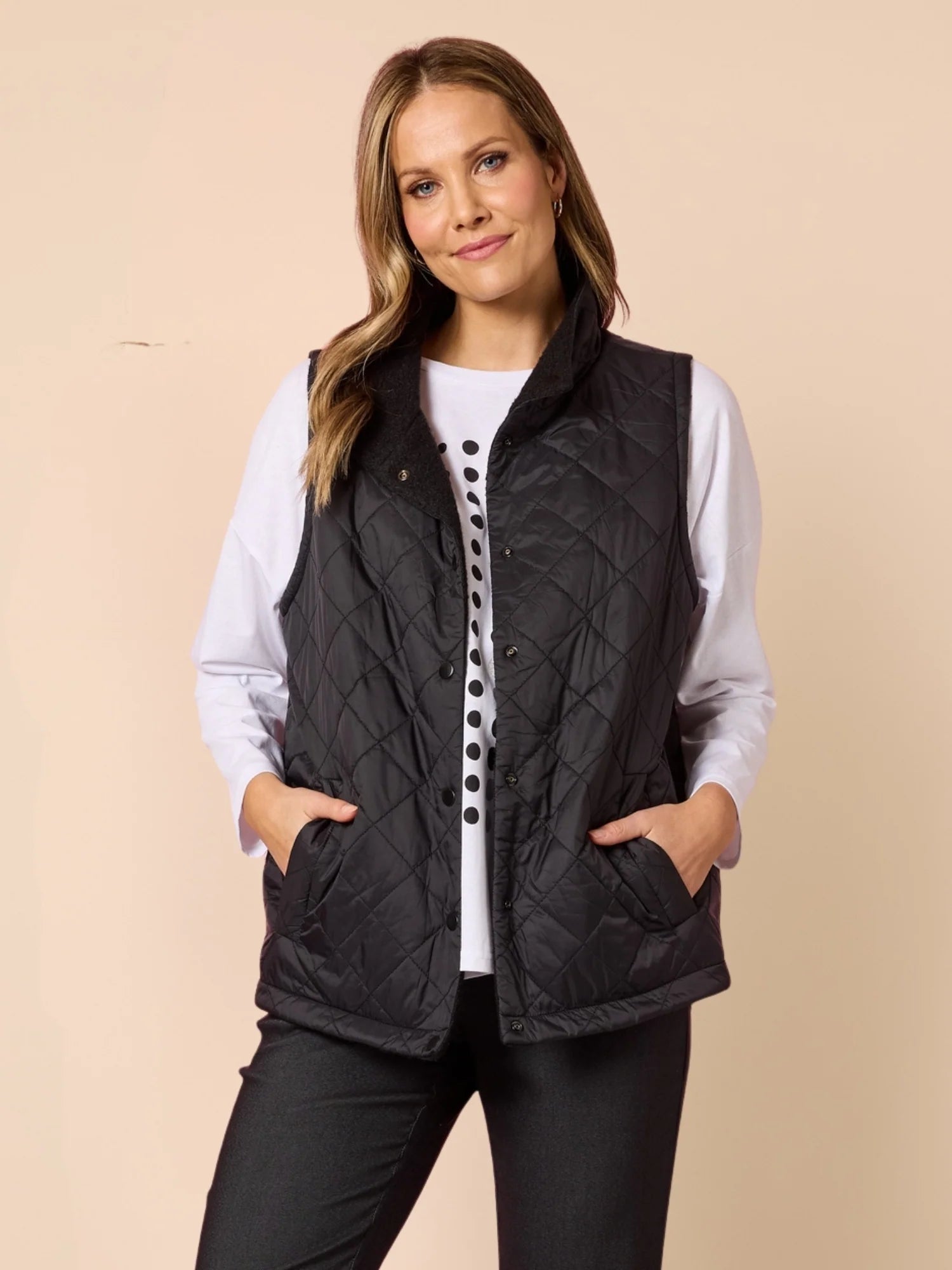 Image of Woman wearing a Clarity black quilted vest over a white shirt on a beige background