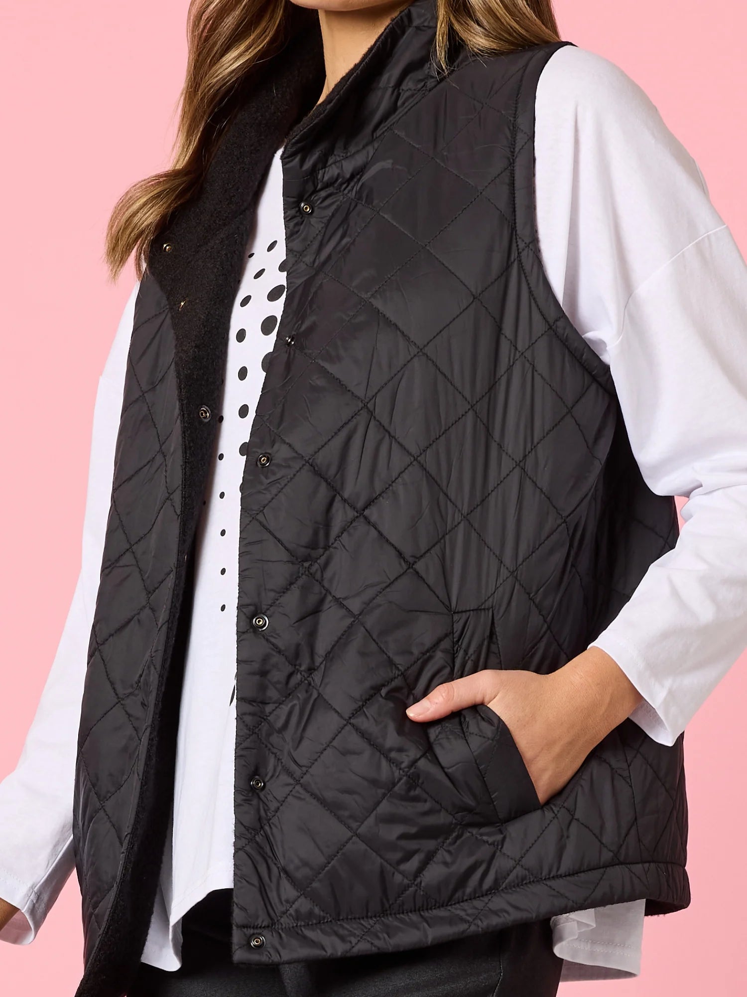 Image of Woman wearing a Clarity black quilted vest over a white shirt with a pink background