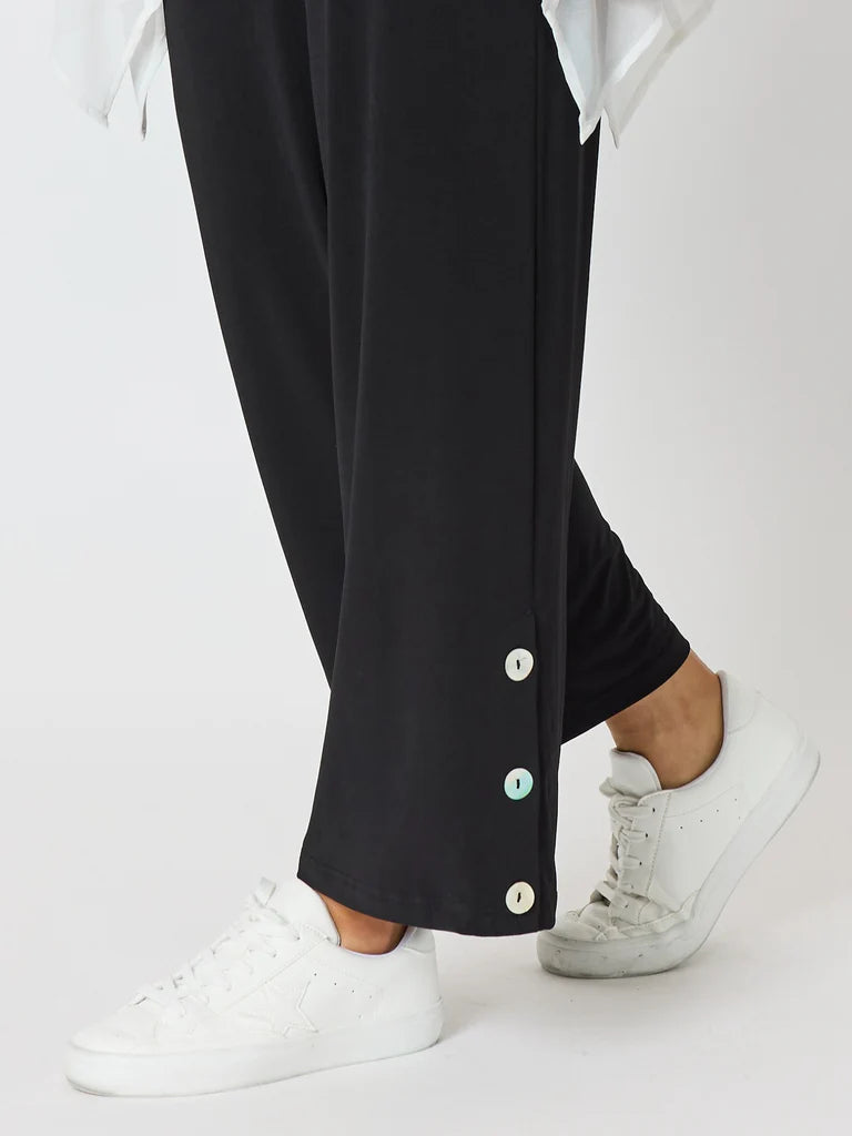 Image of Clarity black wide-leg pants with decorative white, silver, and mint green buttons down the side, shown on a model wearing white sneakers against a light gray background.
