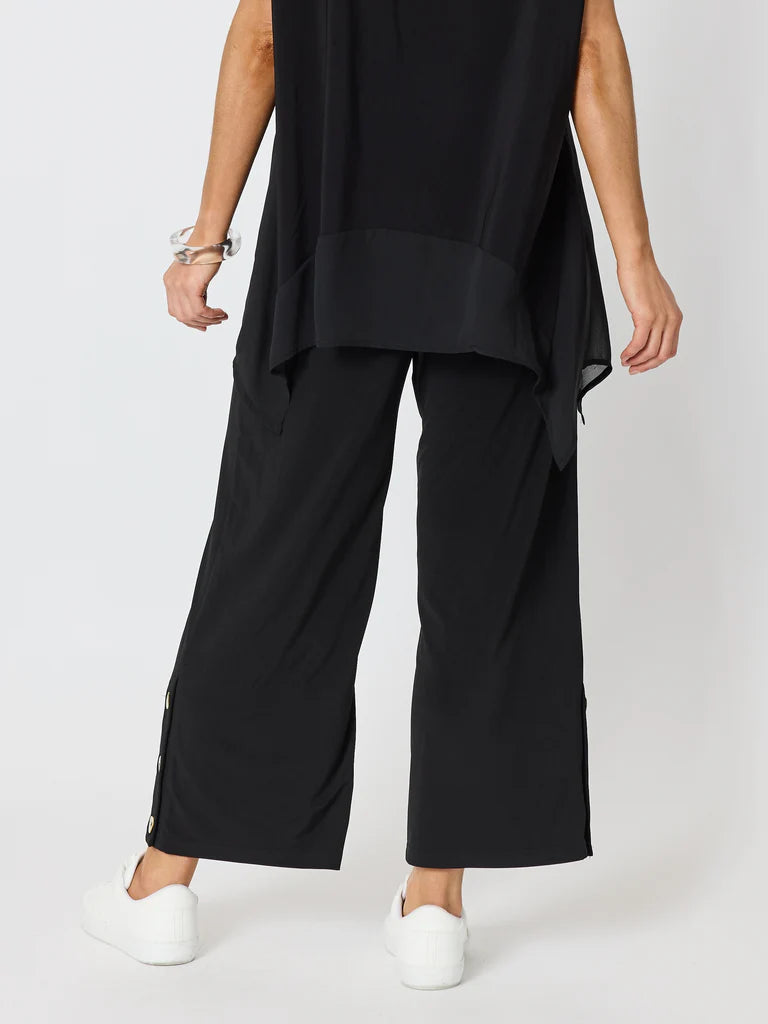Image of A model from the back wearing Clarity black wide-leg cropped pants with side zippers and white sneakers, shown against a light gray studio background.