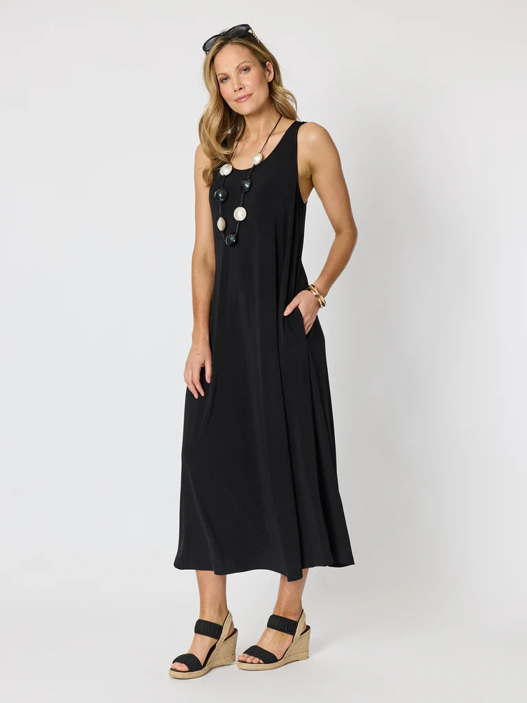 Image of A woman modeling a Clarity sleeveless black midi dress with large decorative white buttons down the front, styled with black wedge sandals and sunglasses on a light gray studio background
